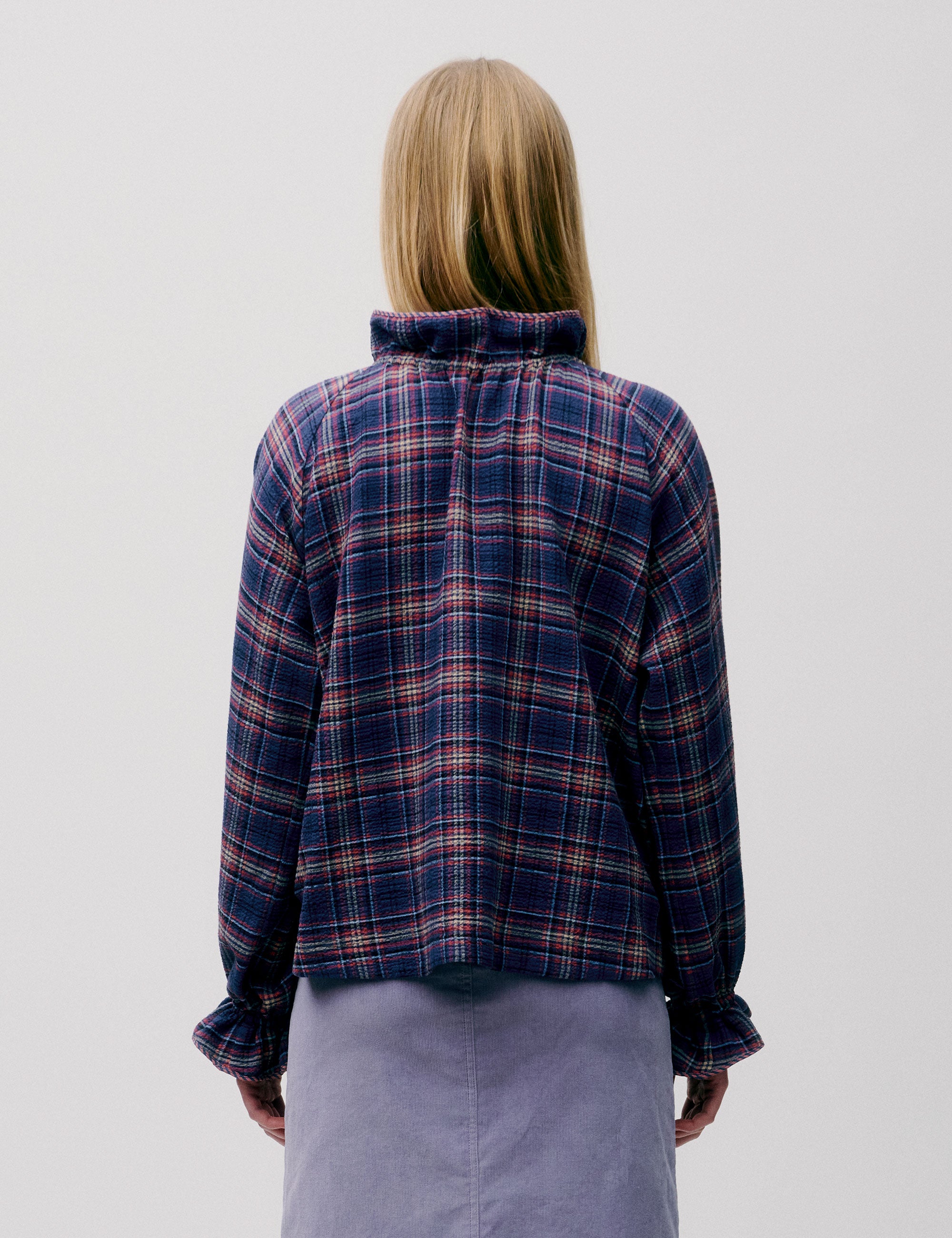 Woman seen from behind wearing a dark checked blouse and light purple skirt.