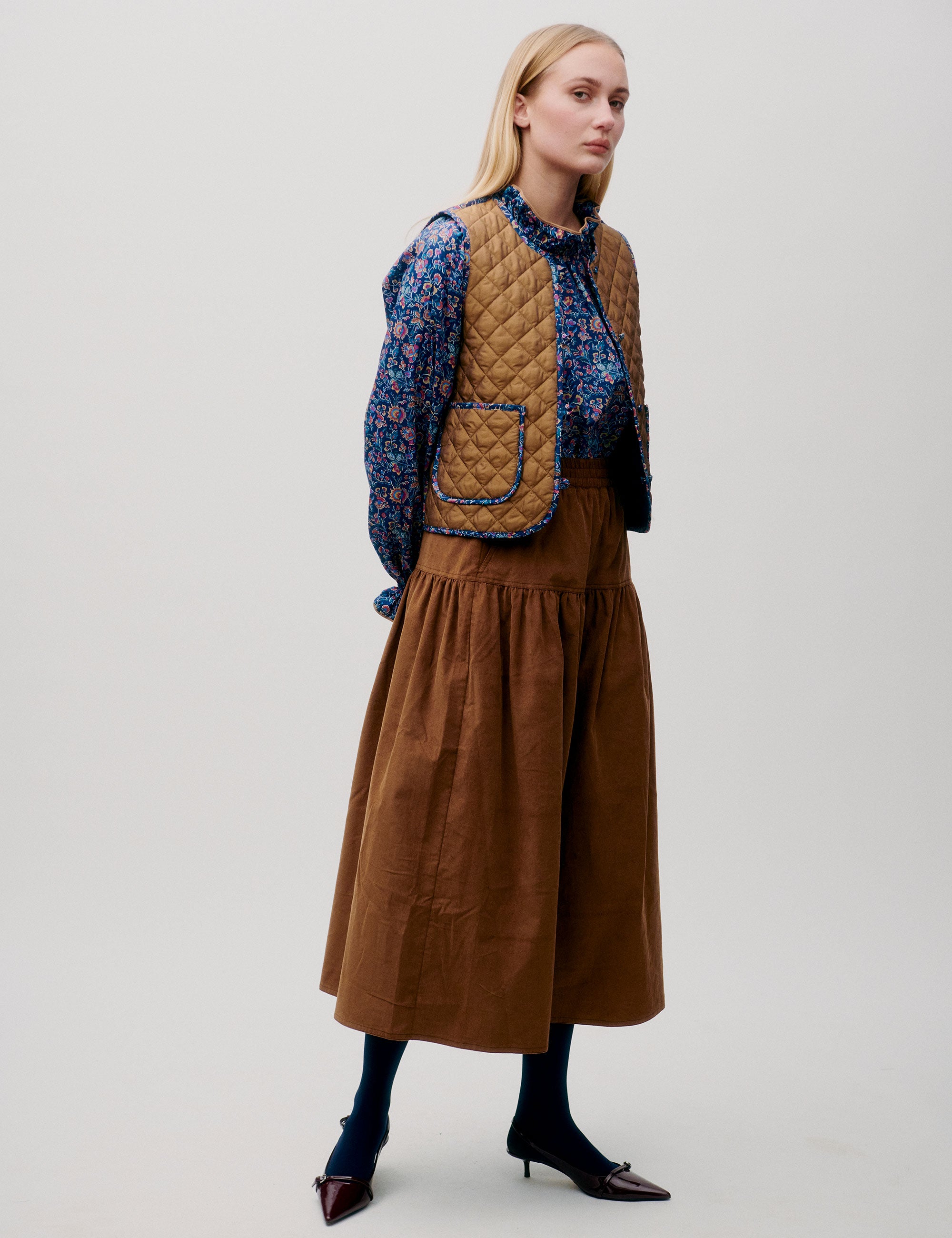 Woman in cognac brown corduroy skirt, floral blouse and quilted brown vest
