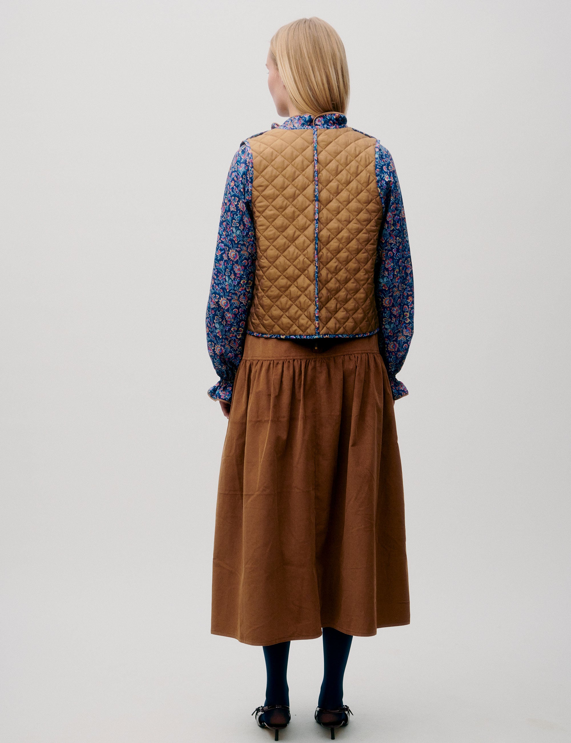 Woman in cognac brown corduroy skirt, floral blouse and quilted brown vest