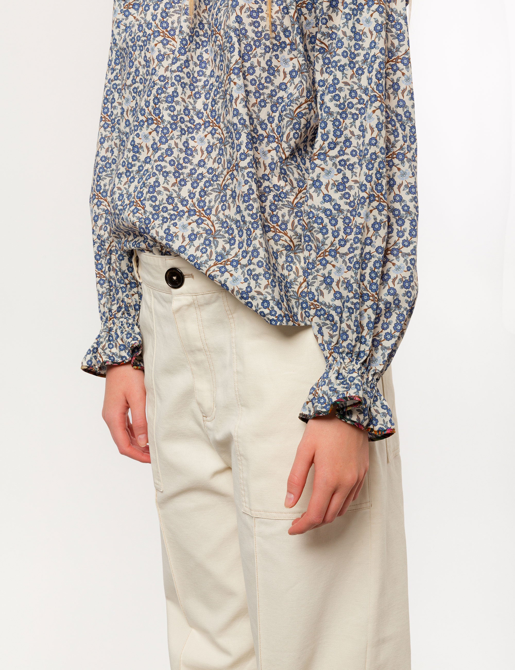 Woman in blue and white floral print liberty cotton shirt with frilled cuffs and collar and creme colored canvas pants