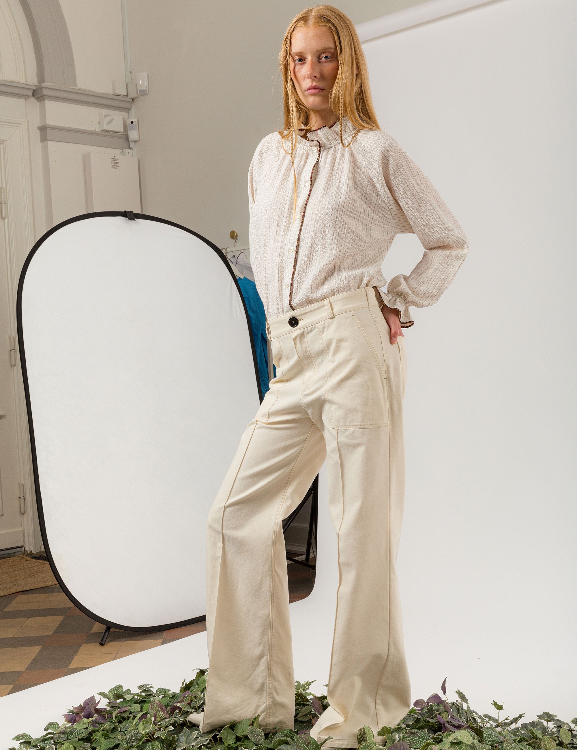 Woman in creme white wide canvas pants and jacket and white striped long-sleeved seersucker shirt with frilled collar and cuffs