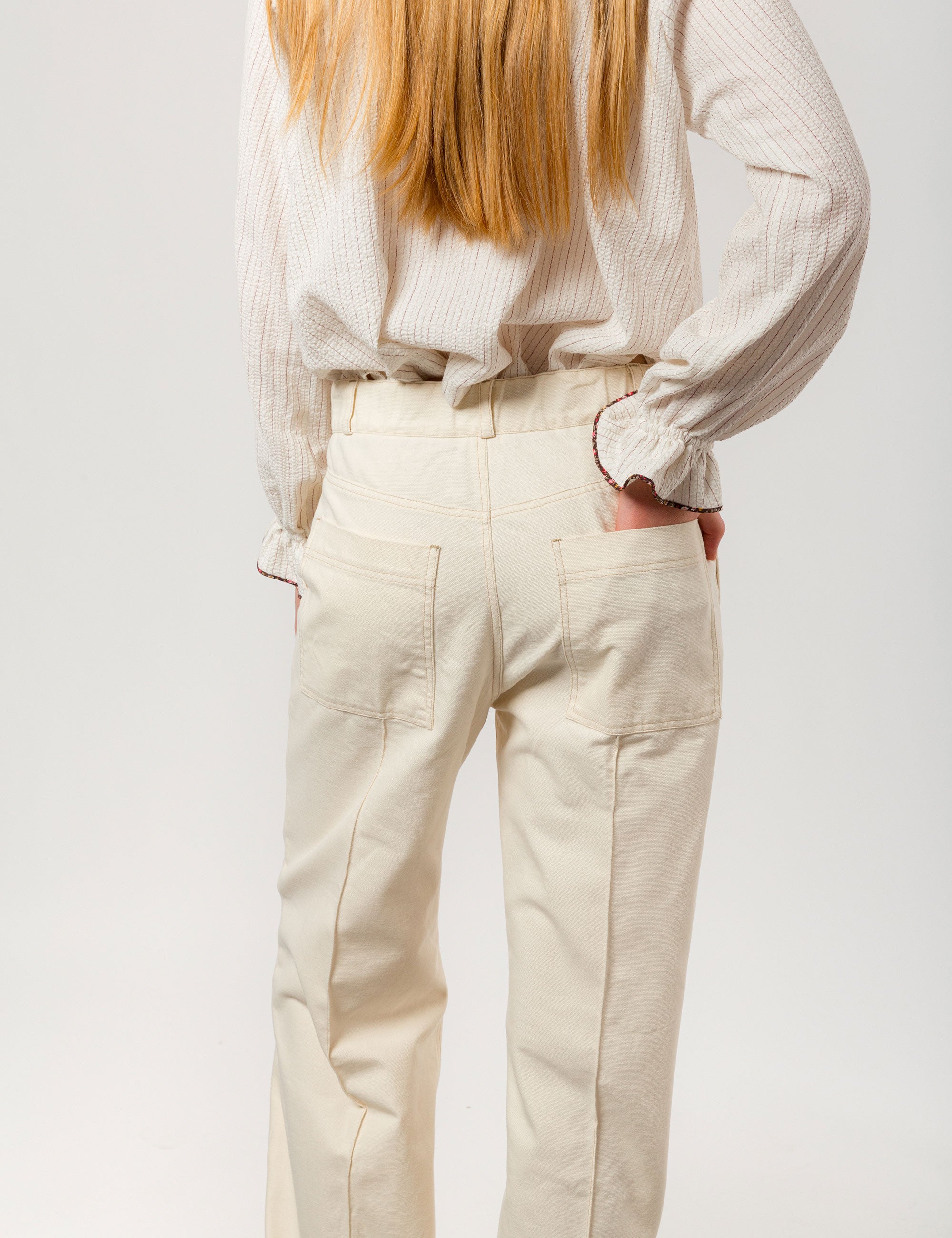 Woman in creme white wide canvas pants and jacket and white striped long-sleeved seersucker shirt with frilled collar and cuffs
