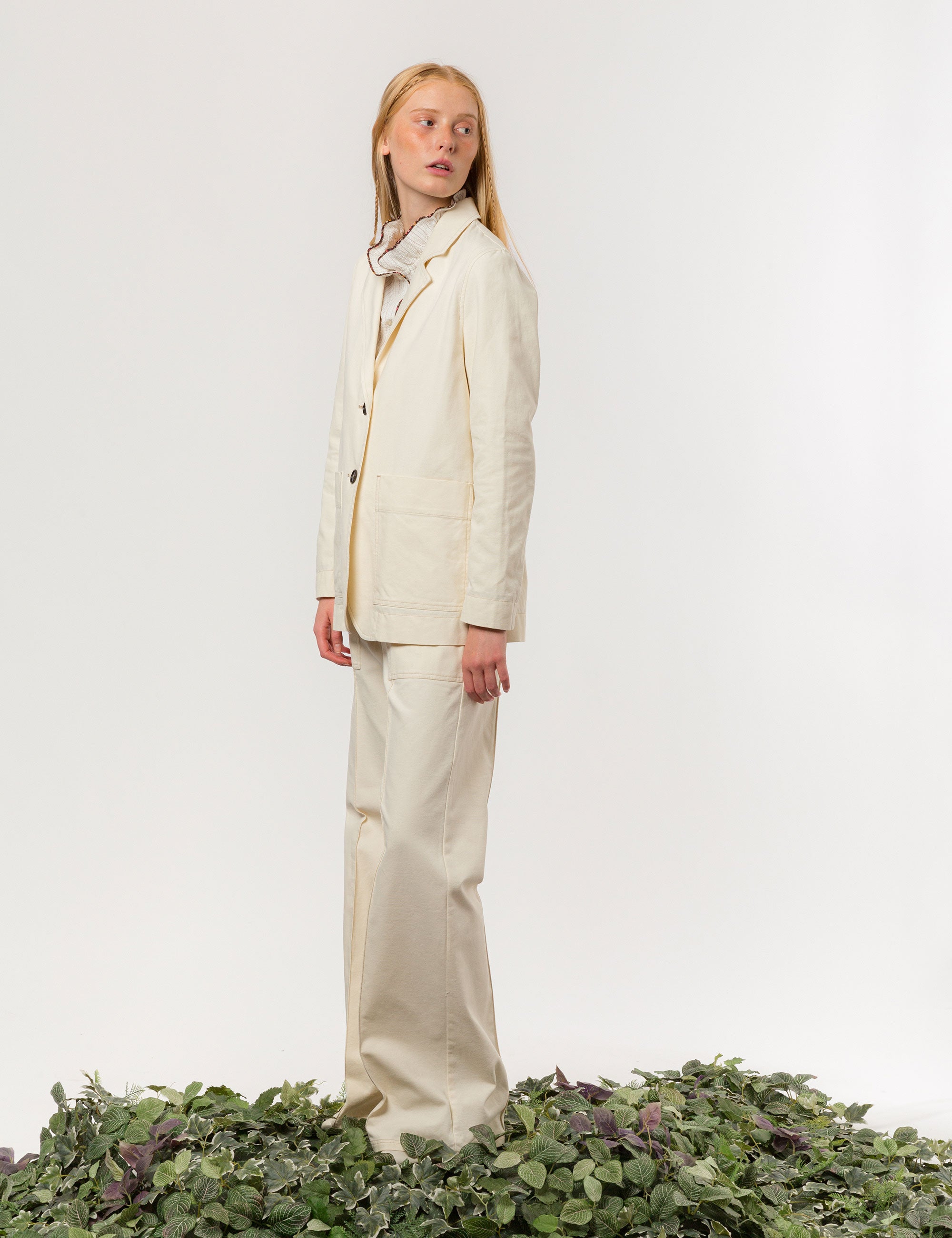 Woman in cream colored canvas jacket with large buttons and pockets and matching wide pants and blouse with contrasting pipings