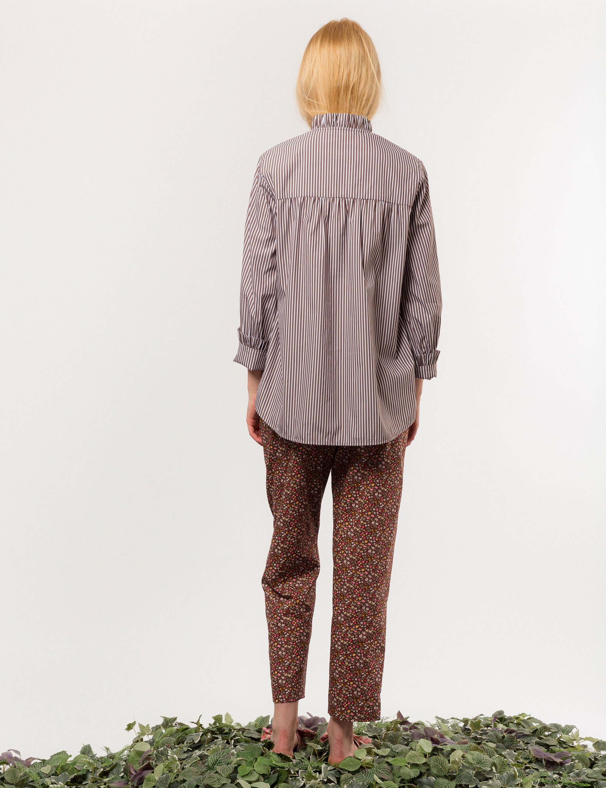 Woman in relaxed pants in liberty cotton brown and red small floral print and brown and white striped long-sleeved cotton shirt with frilled collar and cuffs