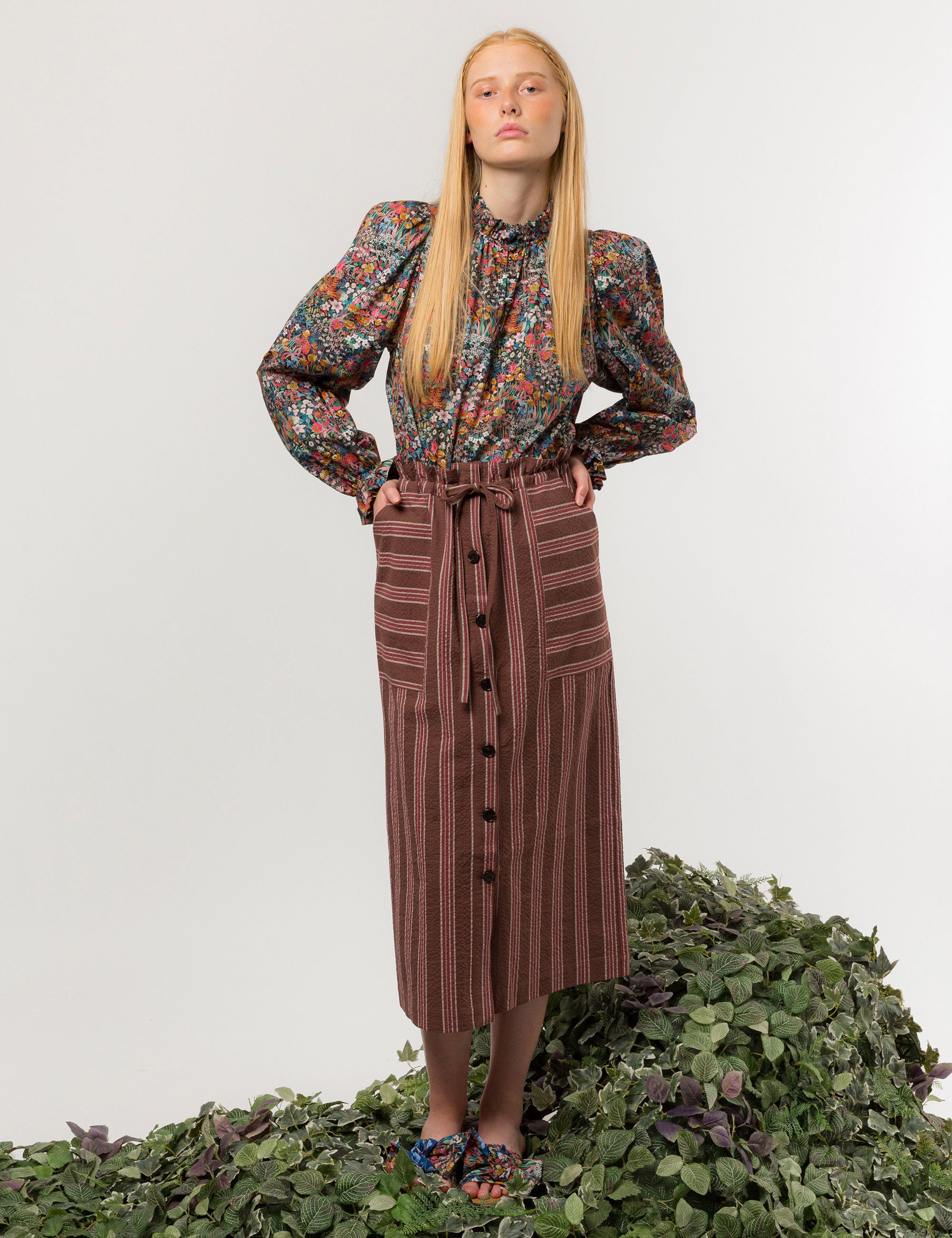Woman in liberty cotton multi-colored floral print shirt with frilled cuffs and collar and brown striped skirt