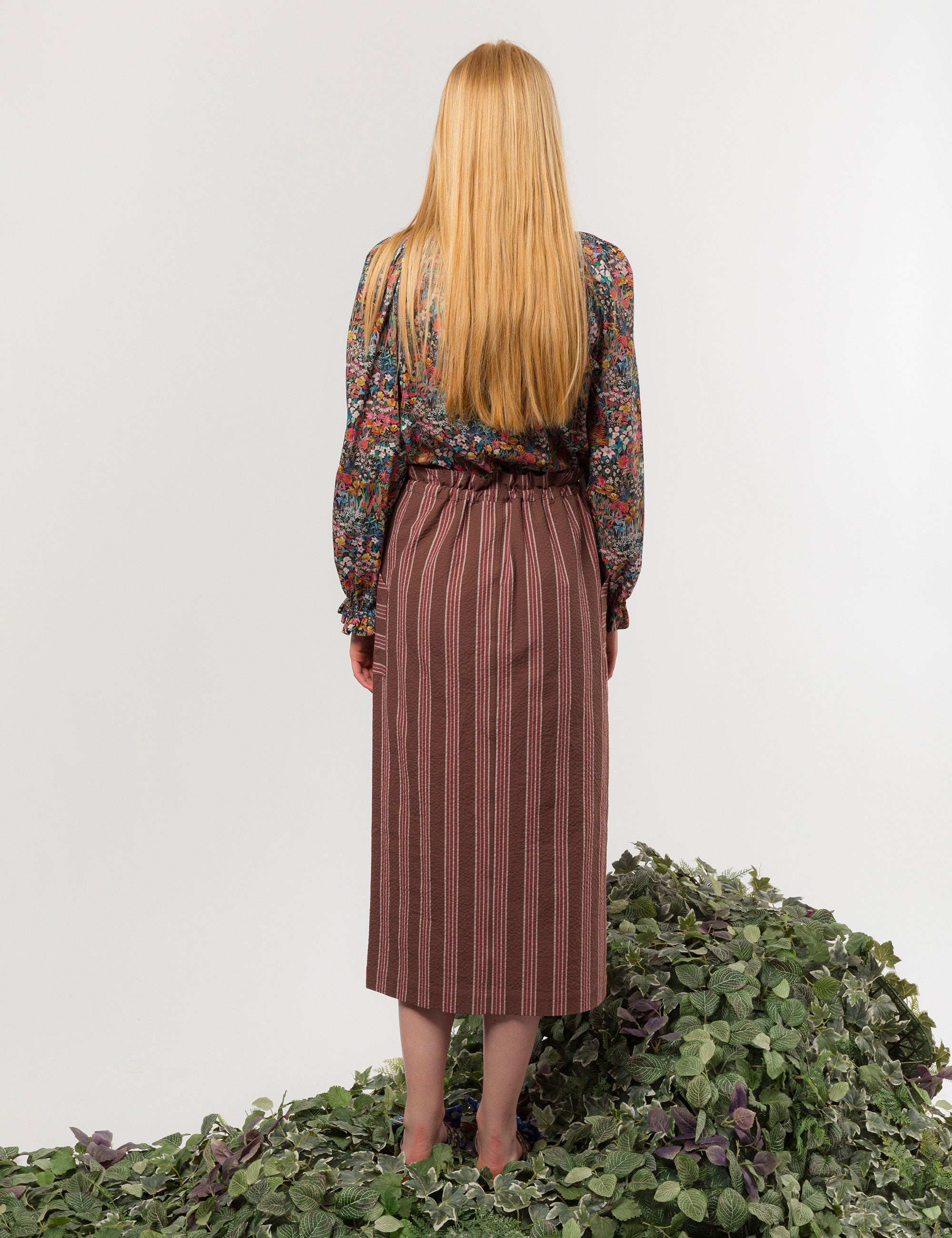 Woman in liberty cotton multi-colored floral print shirt with frilled cuffs and collar and brown striped skirt