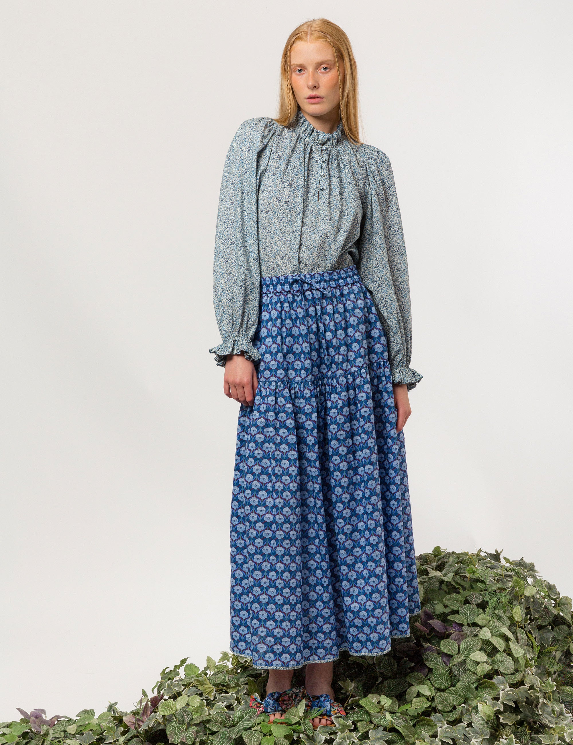 Woman in liberty cotton small blue floral print shirt with frilled cuffs and collar and long sleeves and blue floral skirt