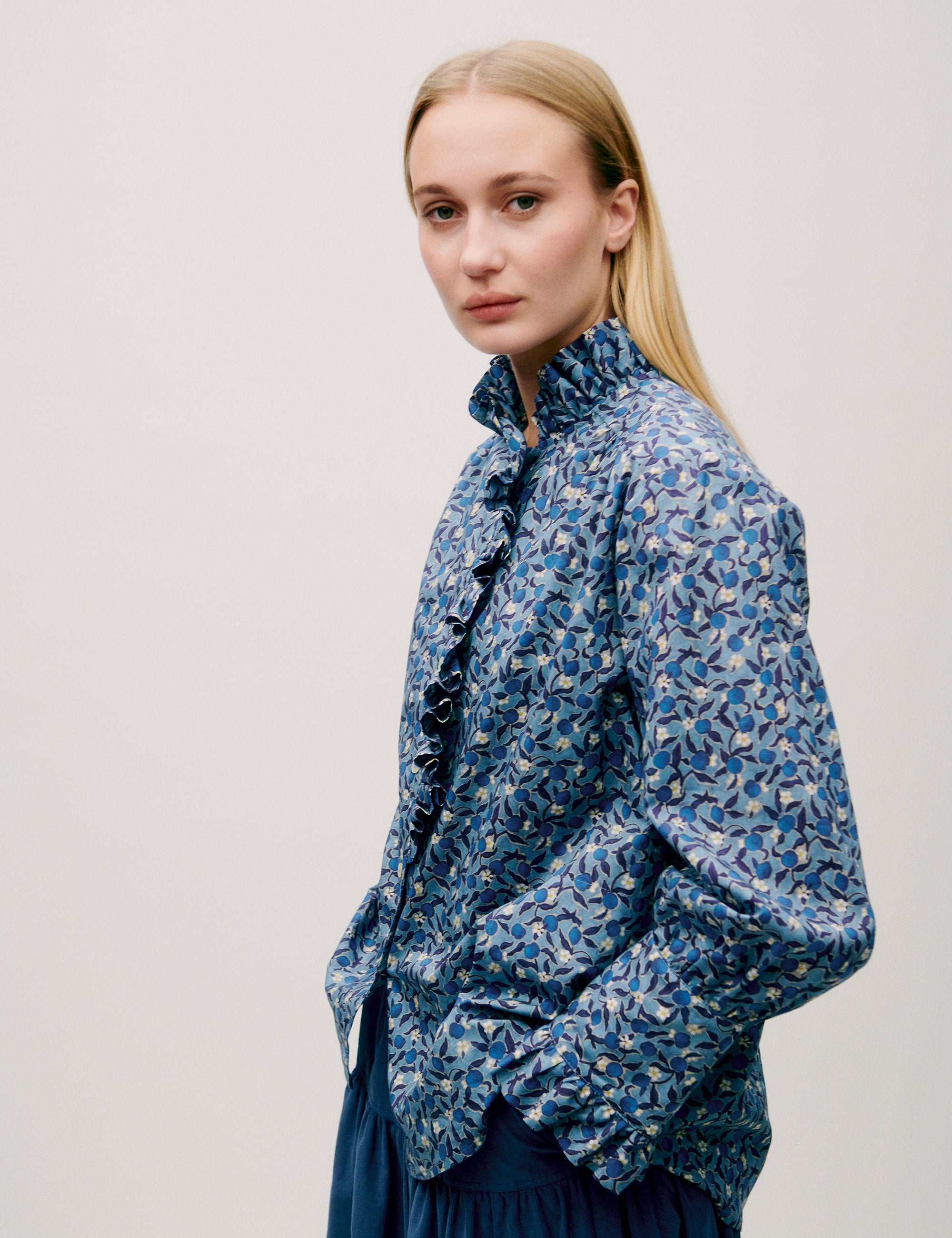 Front view of model wearing a blue floral blouse with ruffled collar