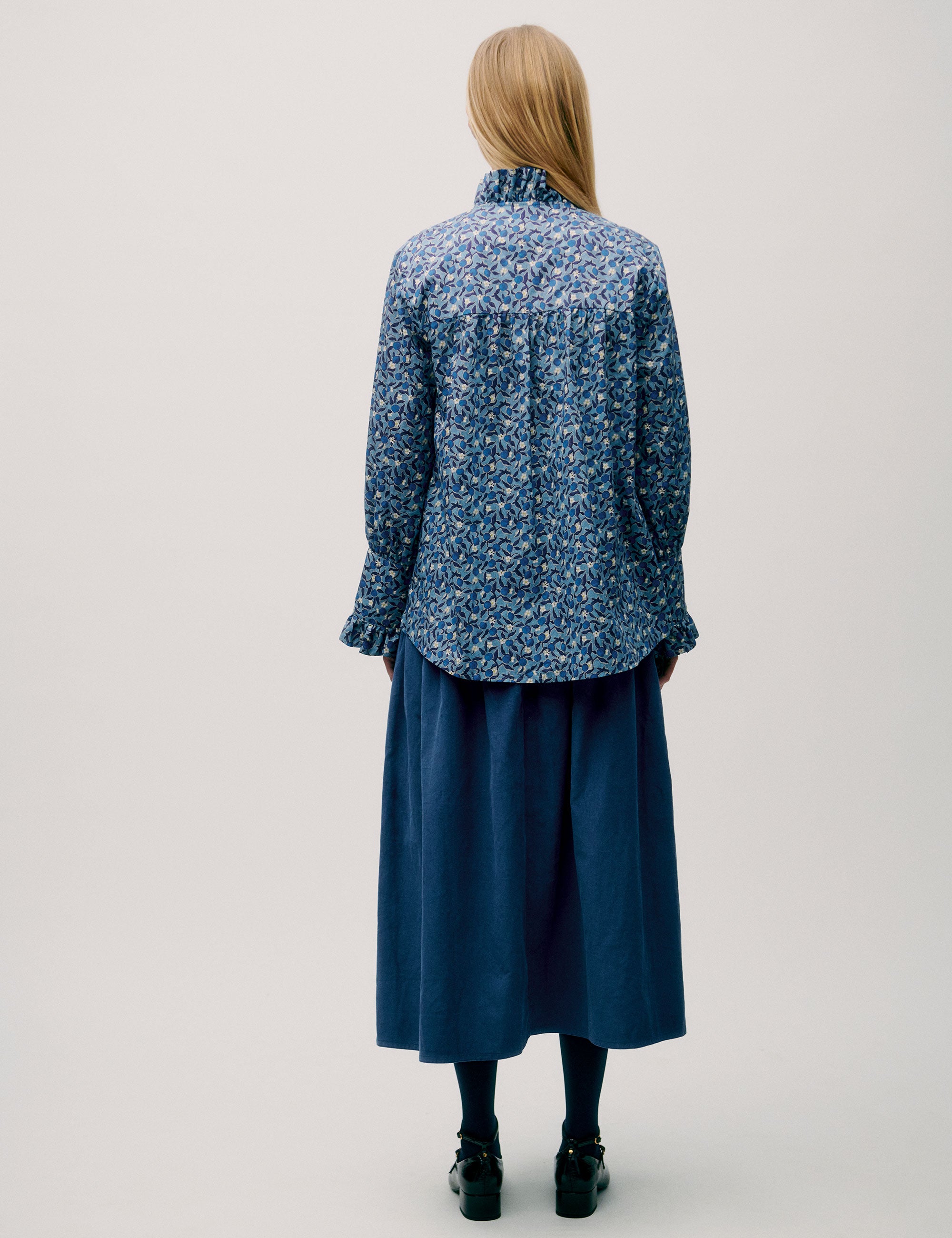 Back view of woman wearing a blue floral blouse with pleated details