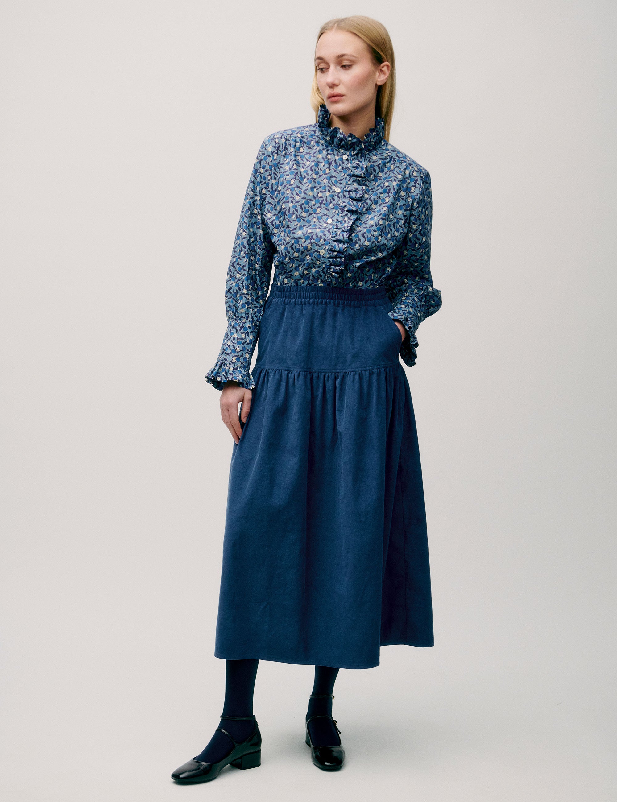 Woman in long blue corduroy skirt and blue floral long sleeved blouse with ruffled neck and cuffs