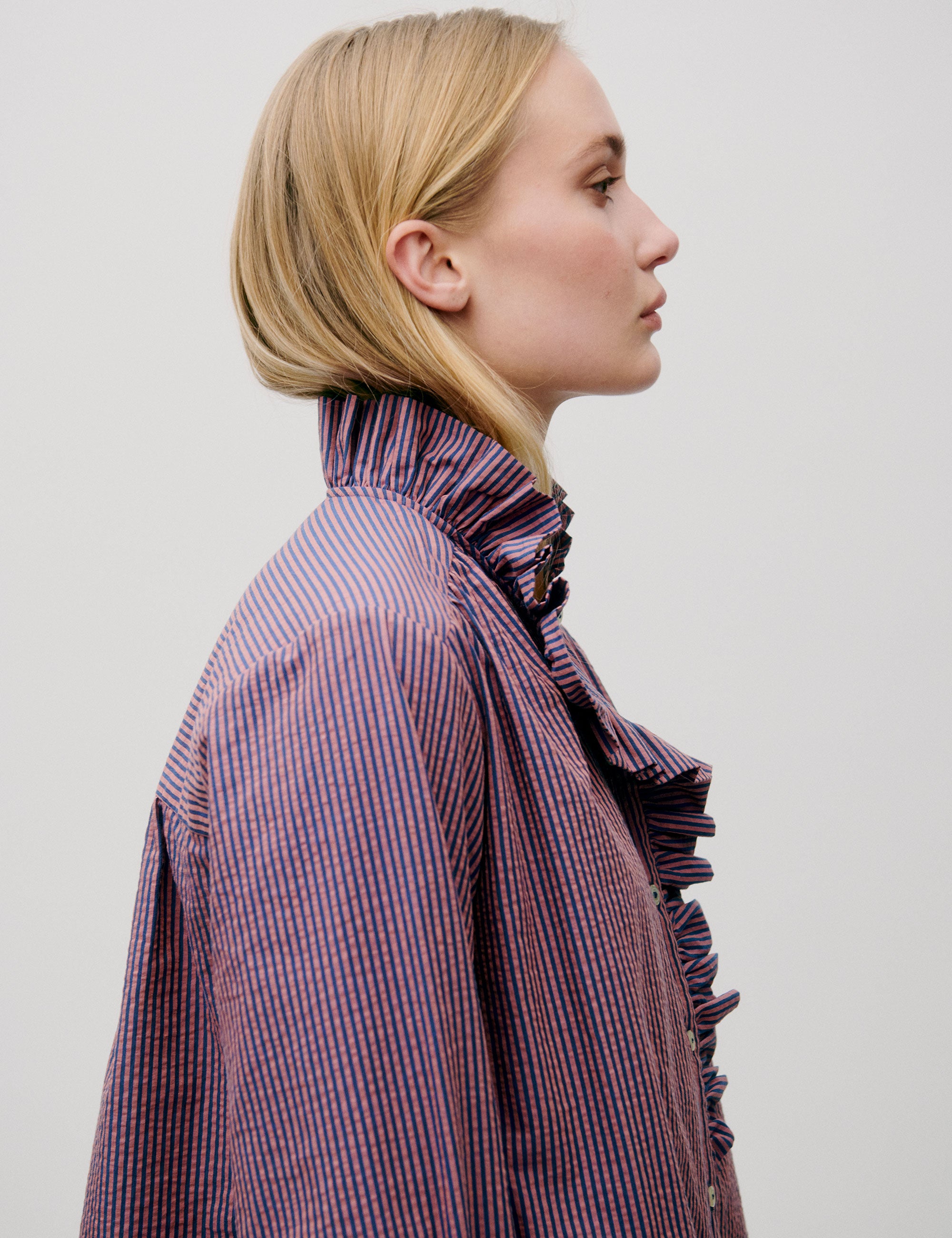 Woman in pink striped shirt with long sleeves, frilled collar and cuffs