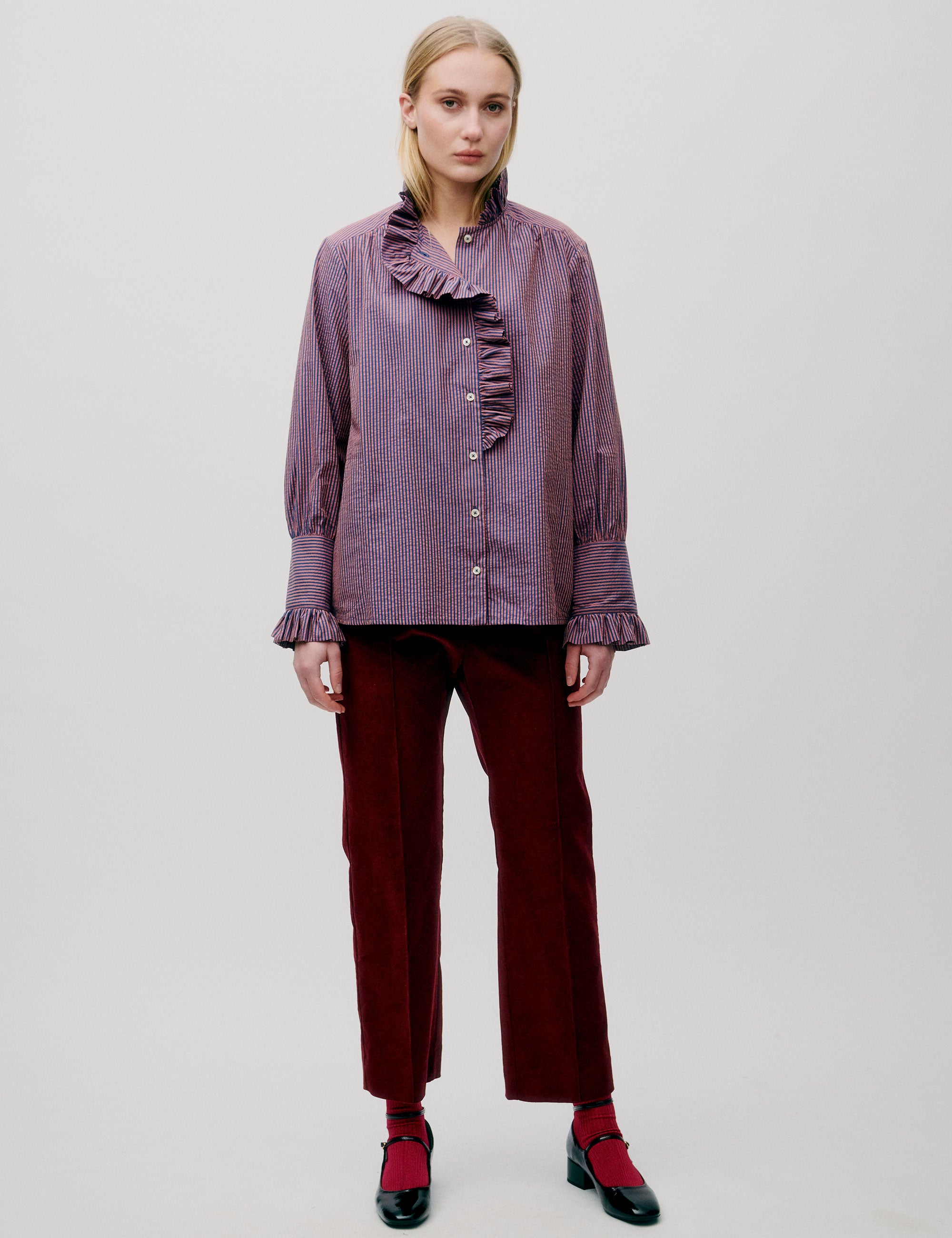 Woman in dark red pants and pink striped shirt with long sleeves, frilled collar and cuffs