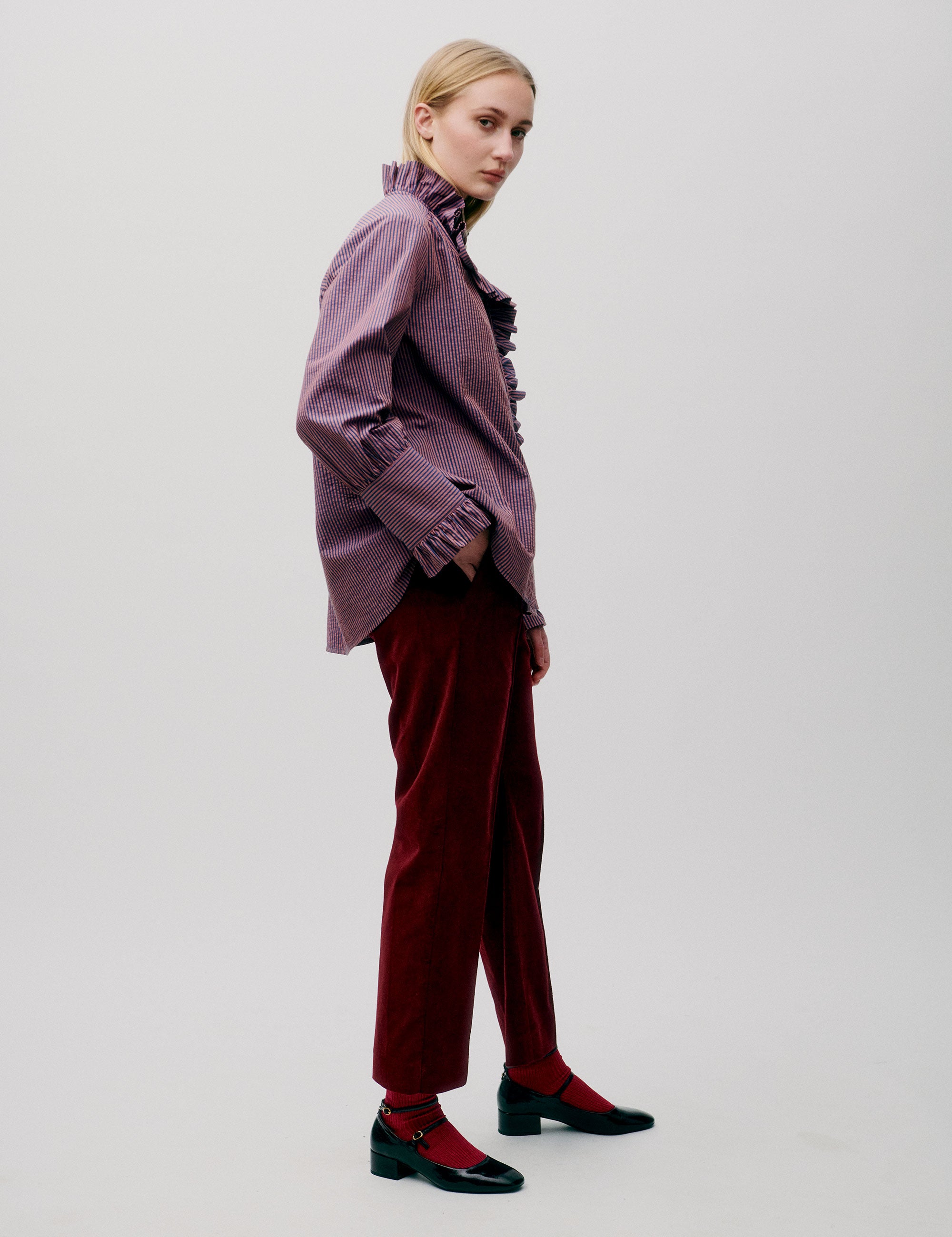 Woman in dark red pants and pink striped shirt with long sleeves, frilled collar and cuffs
