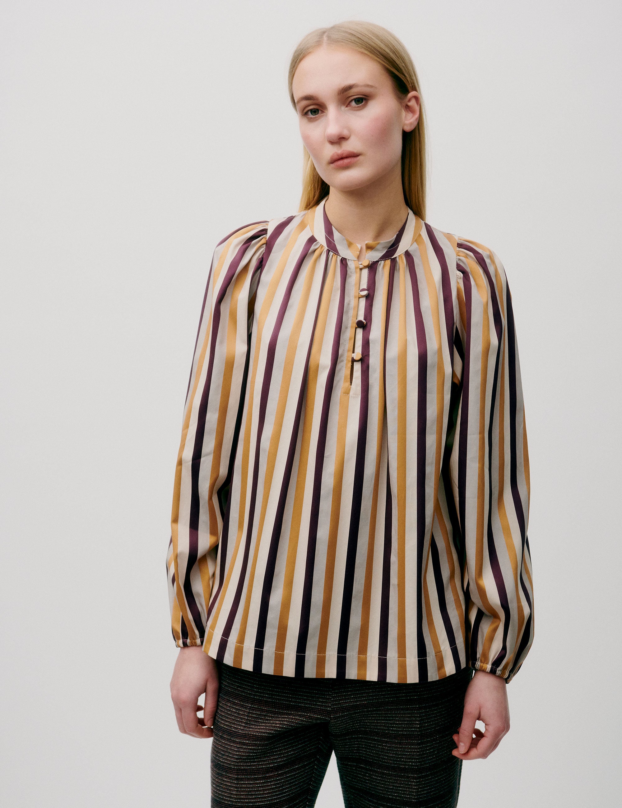 Woman wearing loose-fit striped blouse in mustard, burgundy, and cream tones, front view