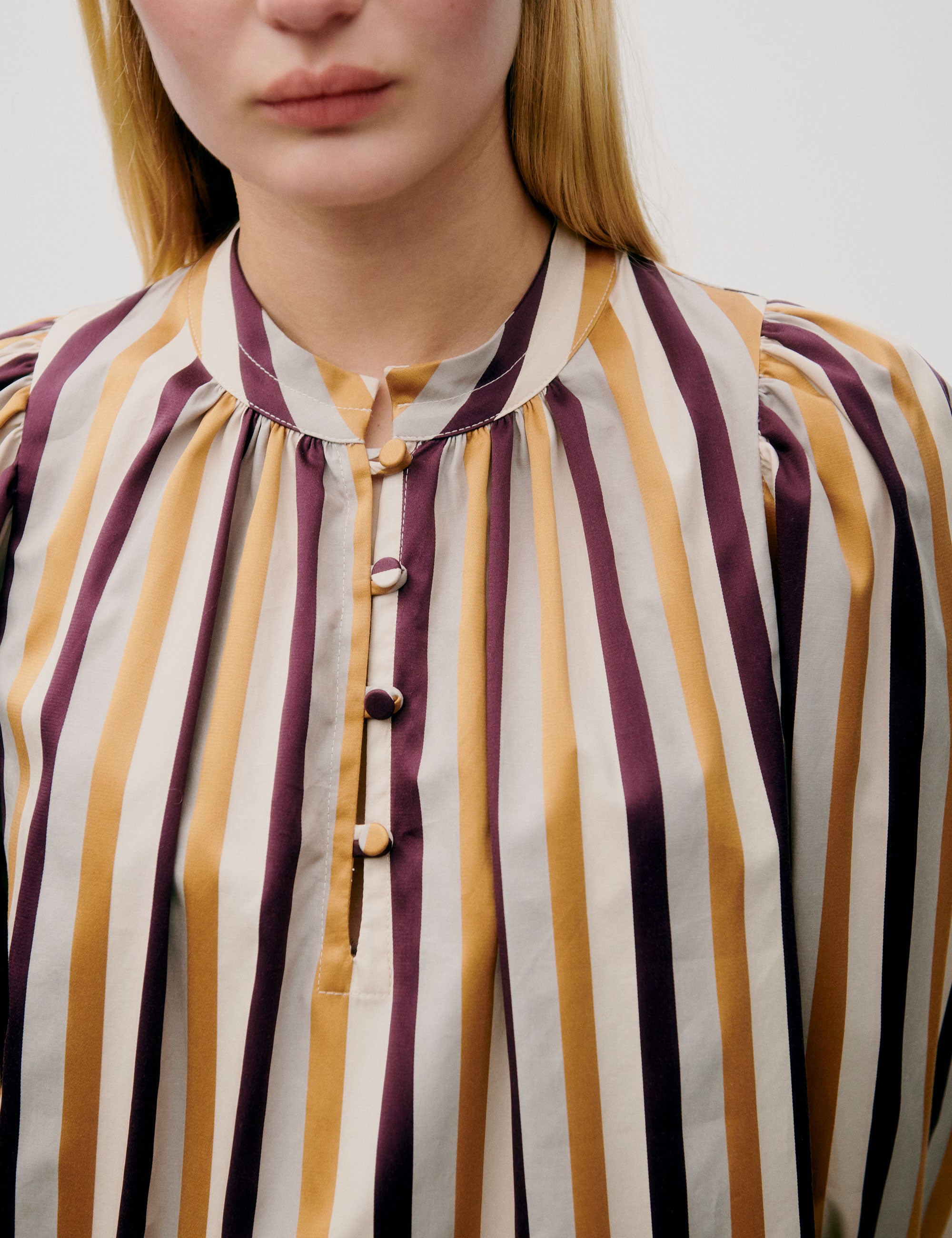 Woman wearing loose-fit striped blouse in mustard, burgundy, and cream tones
