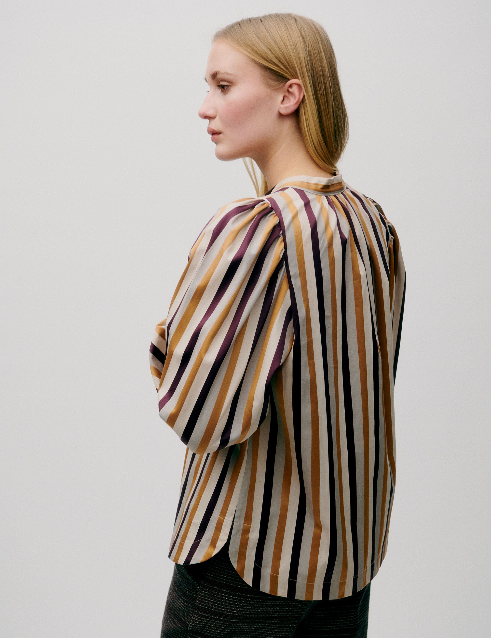 A model wearing a golden stripe shirt with long sleeves and a round neckline.