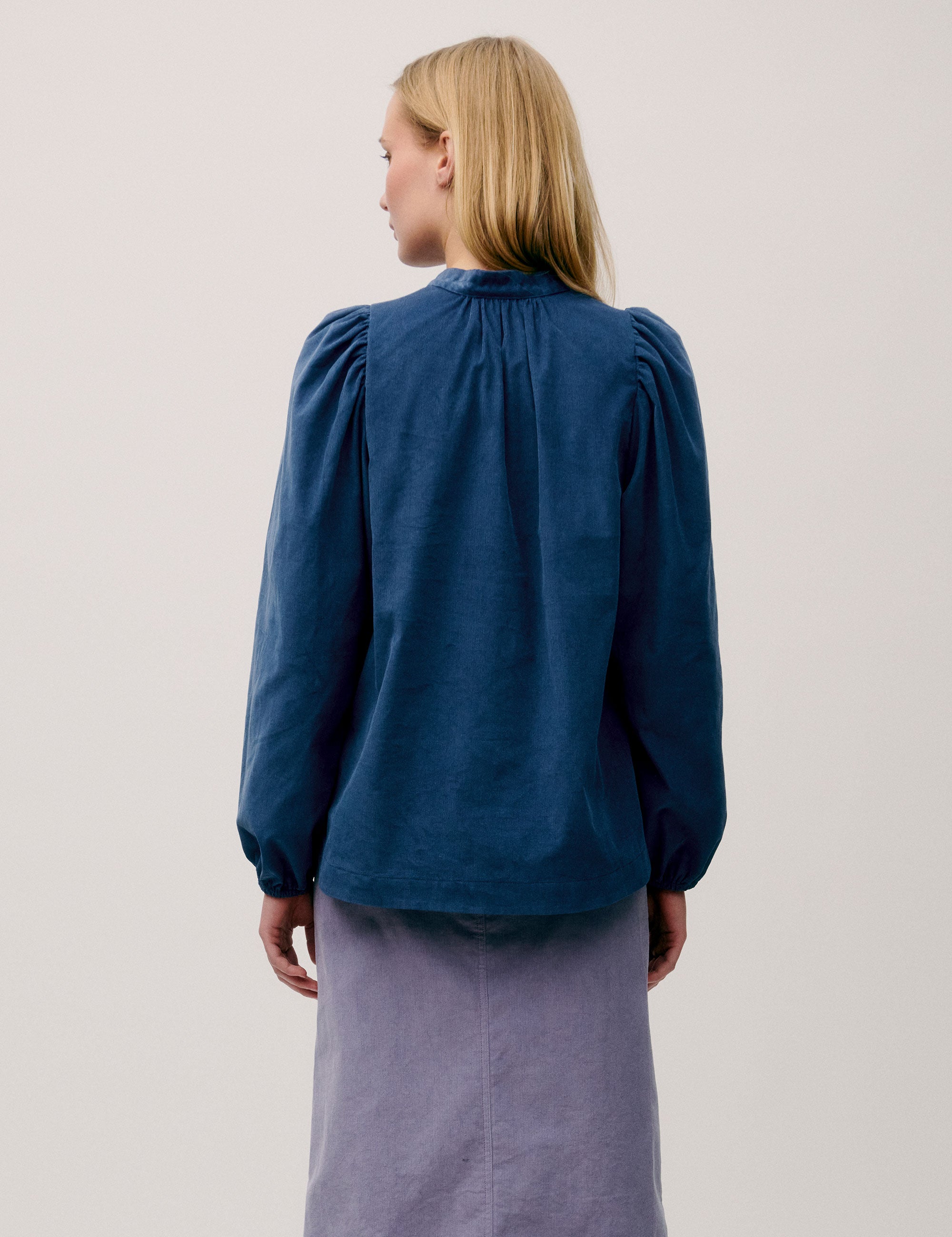 Back view of woman wearing a blue corduroy blouse with gathered detail