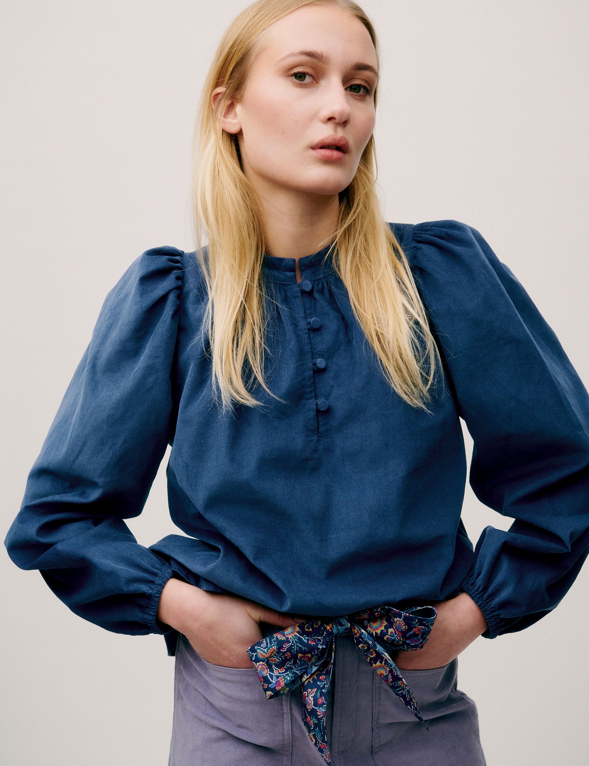 Woman wearing a blue corduroy blouse with puff sleeves and button detail, paired with a lavender skirt