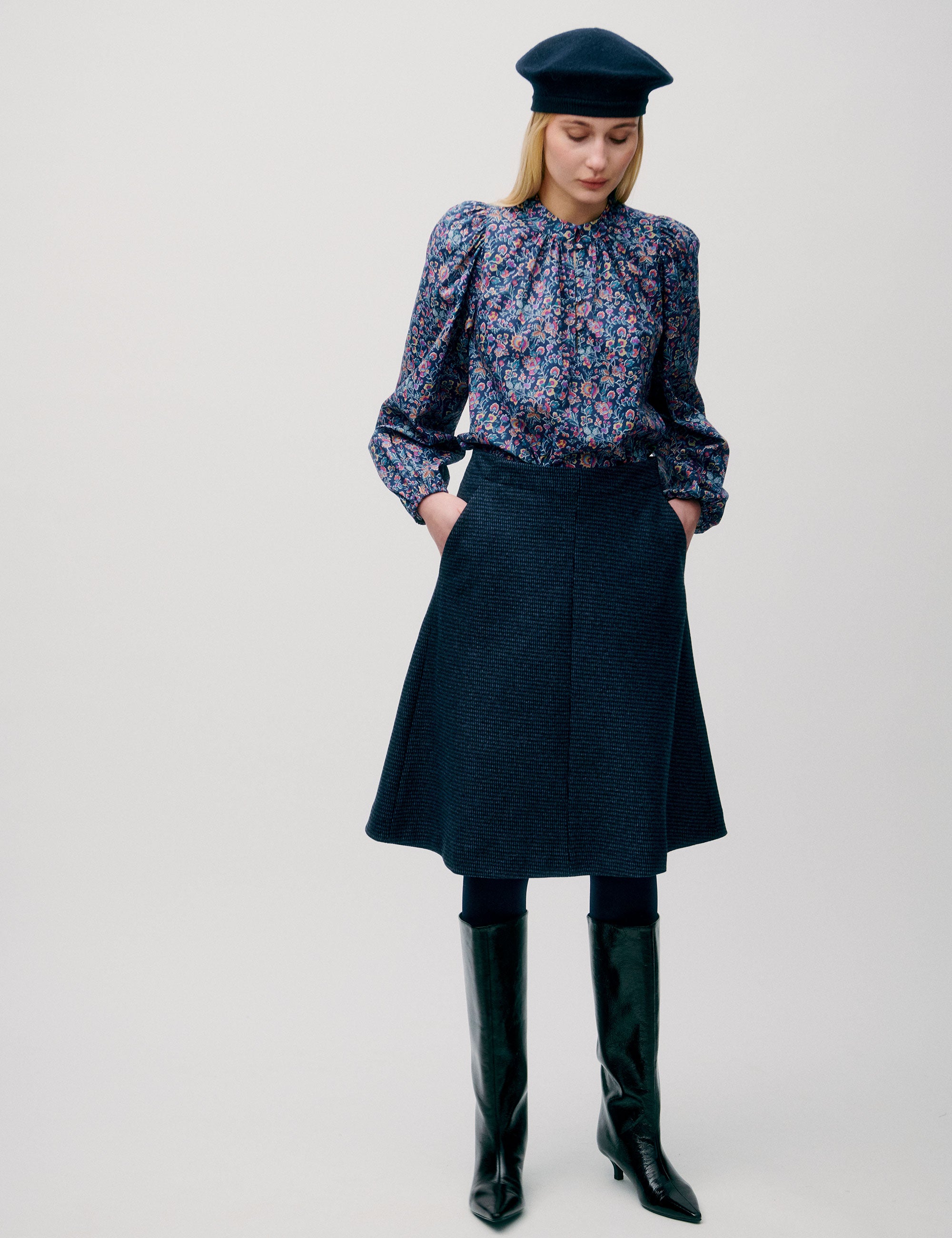 Woman wearing a dark blue tweed A-line skirt styled with a floral blouse, tall boots, and beret