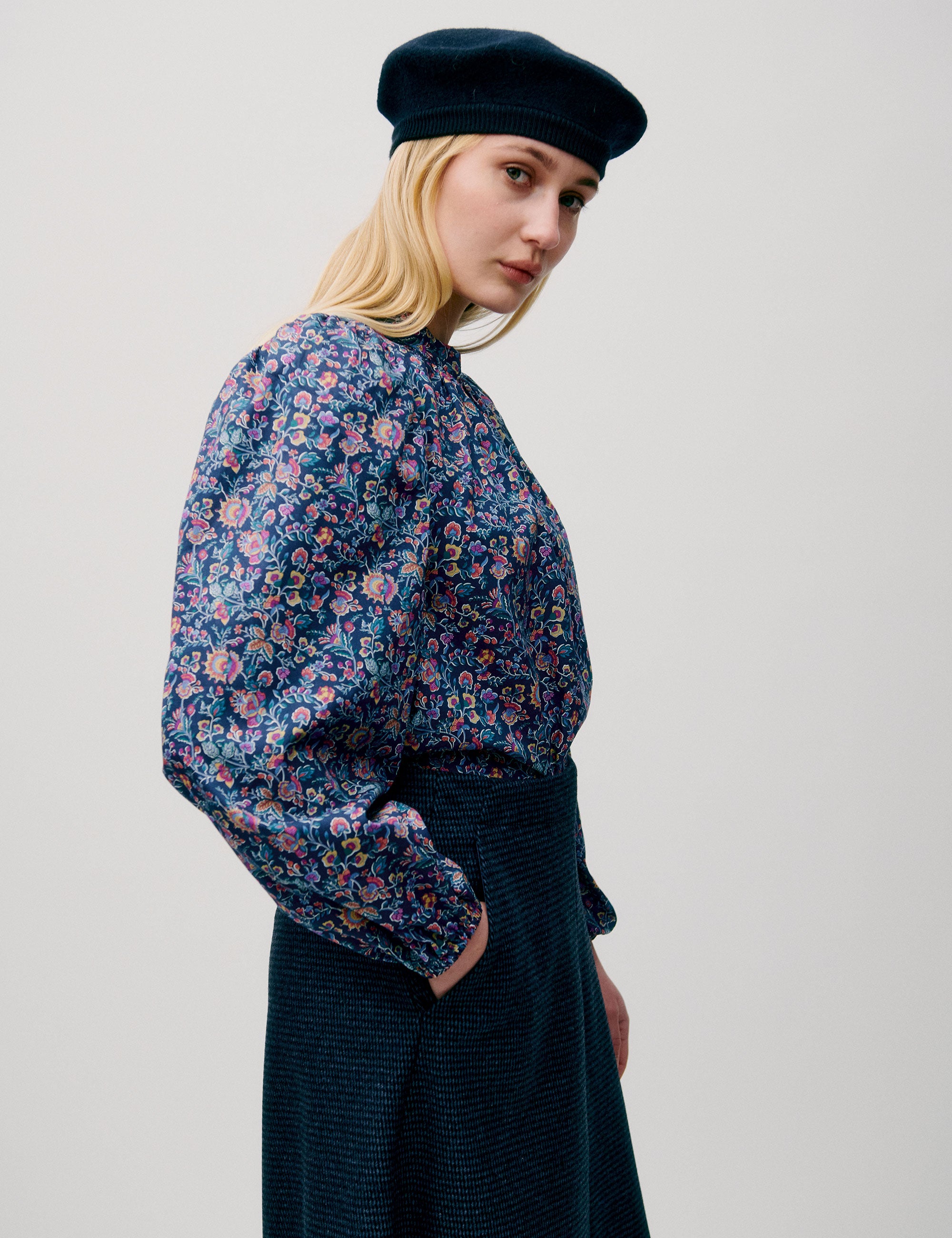 Kvinna i blommig blus med ballongärmar och mörkblå kjol, stylad med basker