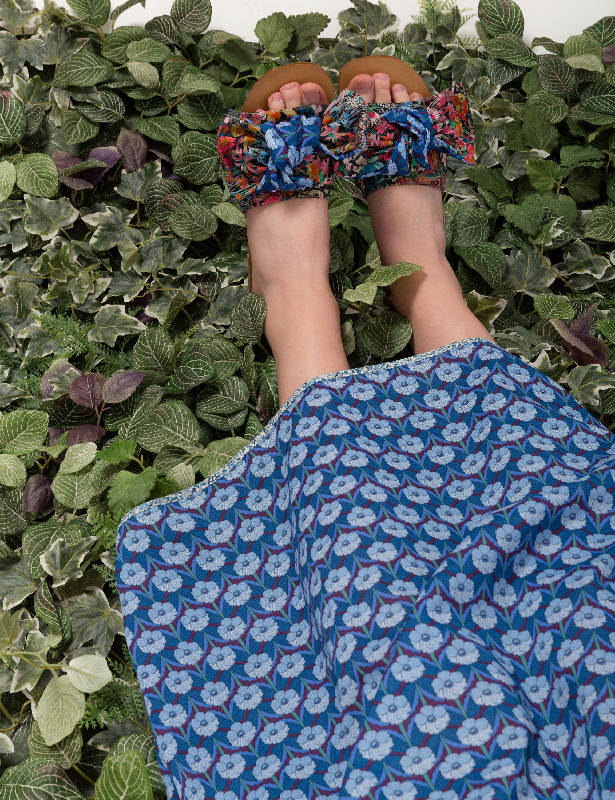 Woman in blue flower print dress and sandals with low heel leather sole and flower patterned bows
