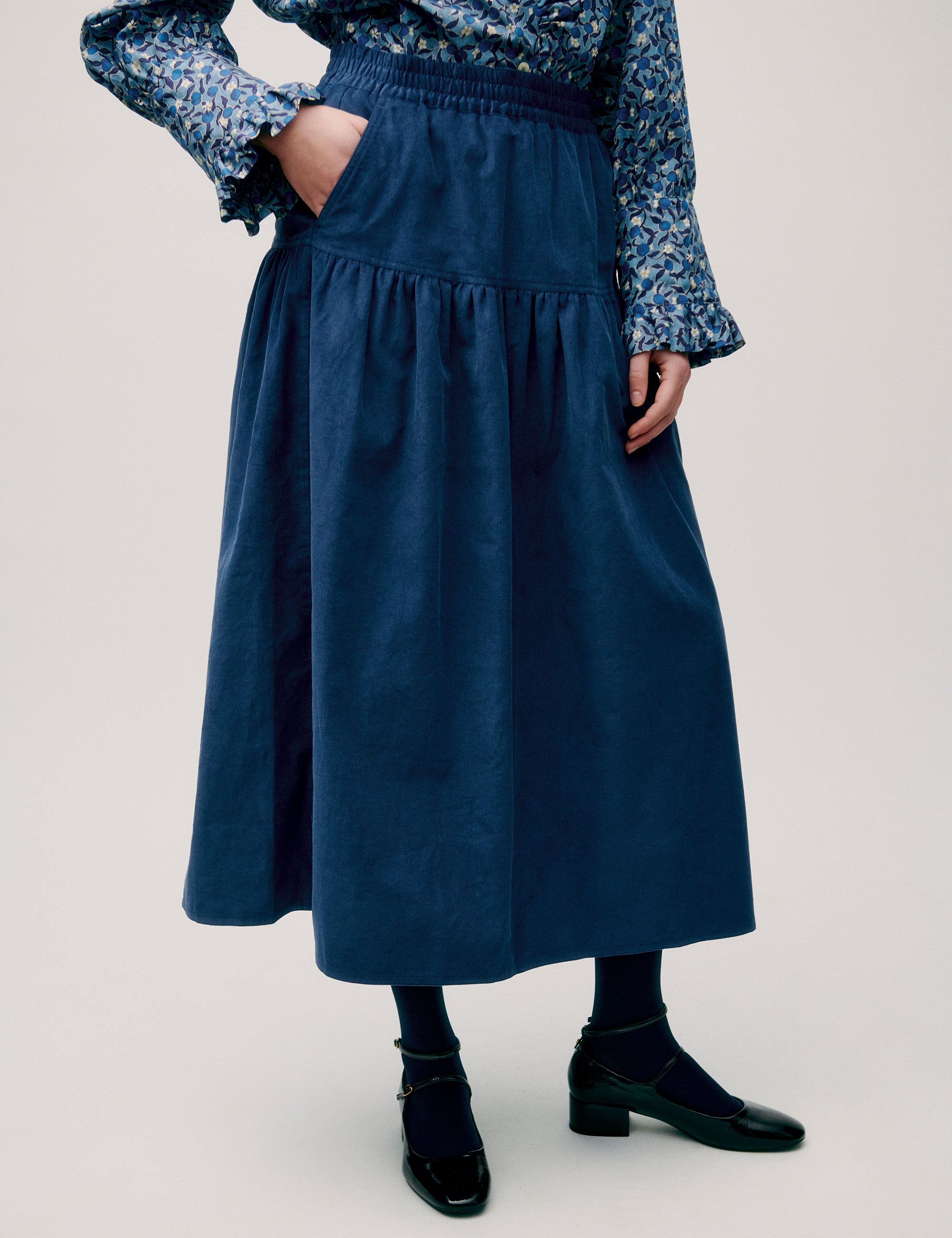 Woman in long blue corduroy skirt and blue floral long sleeved blouse with ruffled neck and cuffs