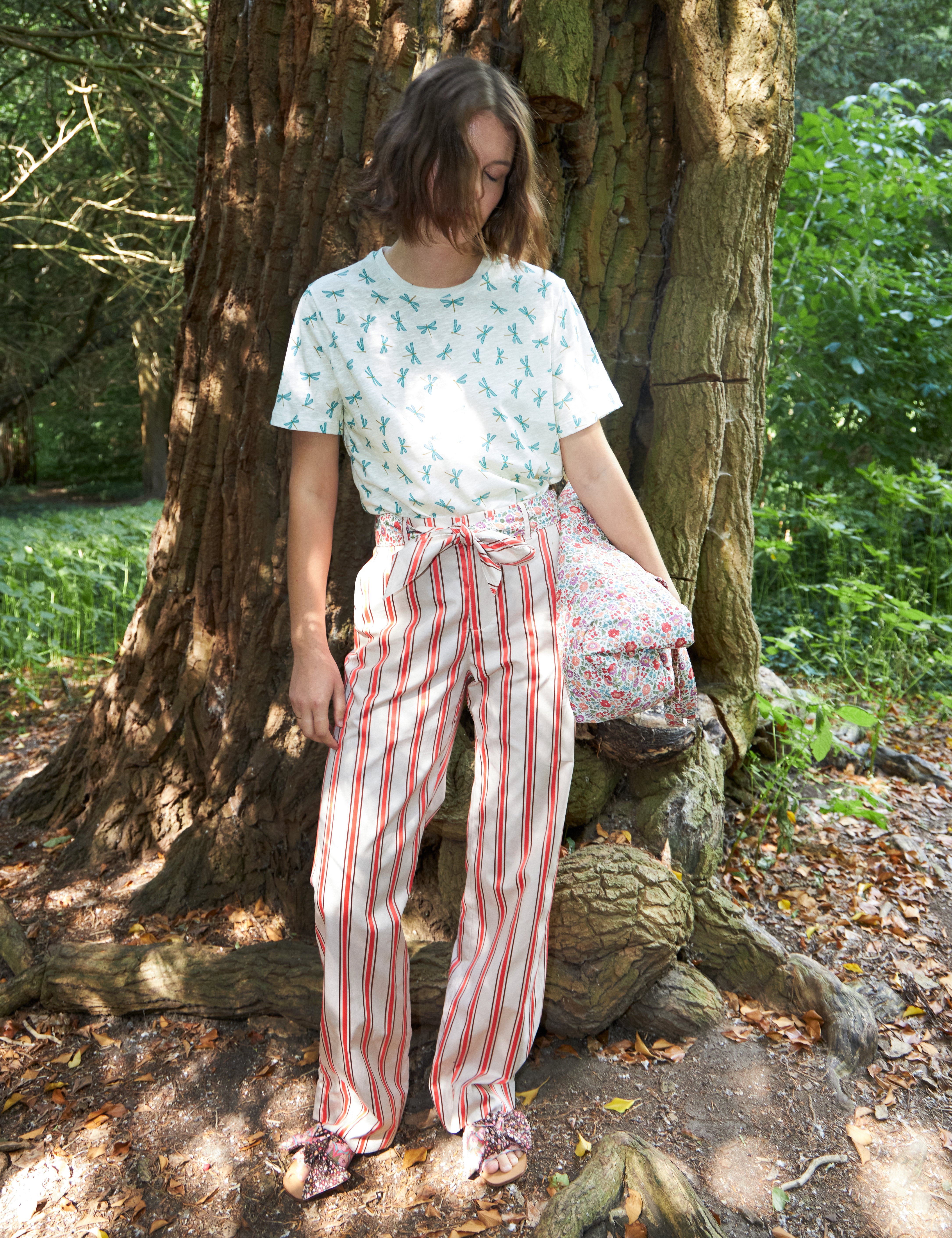 Woman in red and white striped pants with cotton belt and white t-shirt with green dragonfly pattern carrying a multi-colored floral print cotton bag