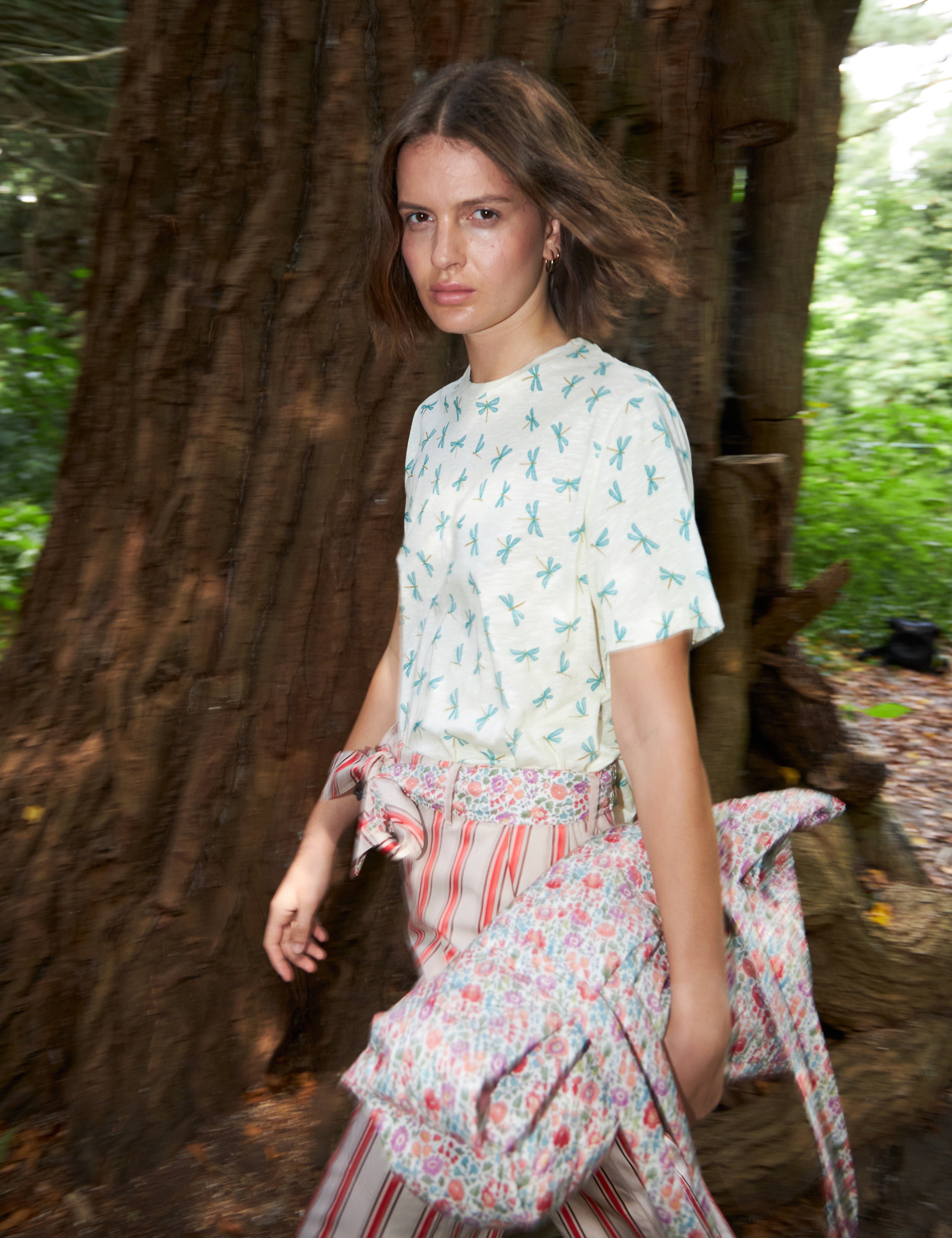 Woman in red and white strped pants with cotton belt and white t-shirt with green dragonfly pattern carrying a multi-colored floral print cotton bag
