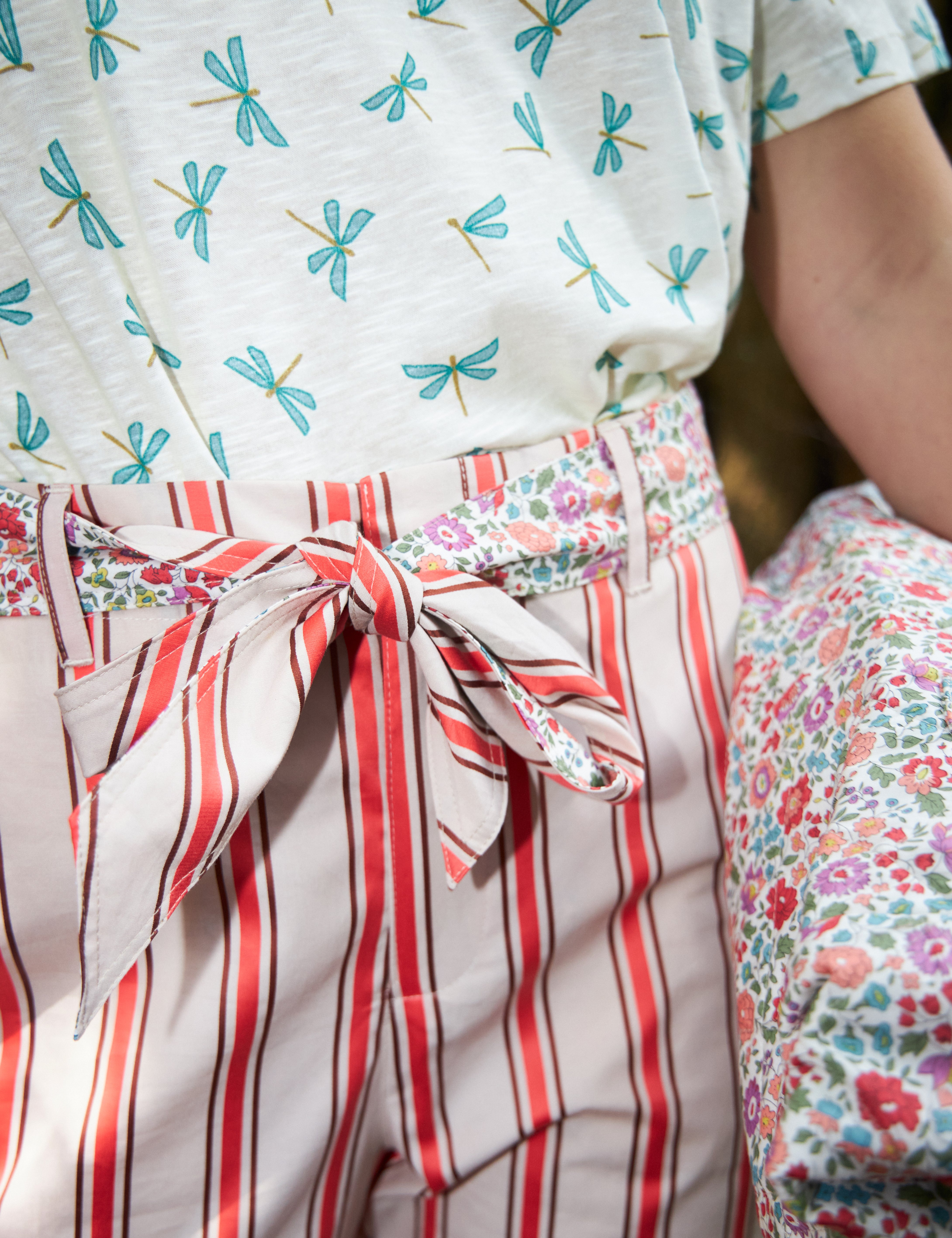 Kvinna i rödvit randiga byxor med bomullsbälte och vit t-shirt med grönt trollsländetryck