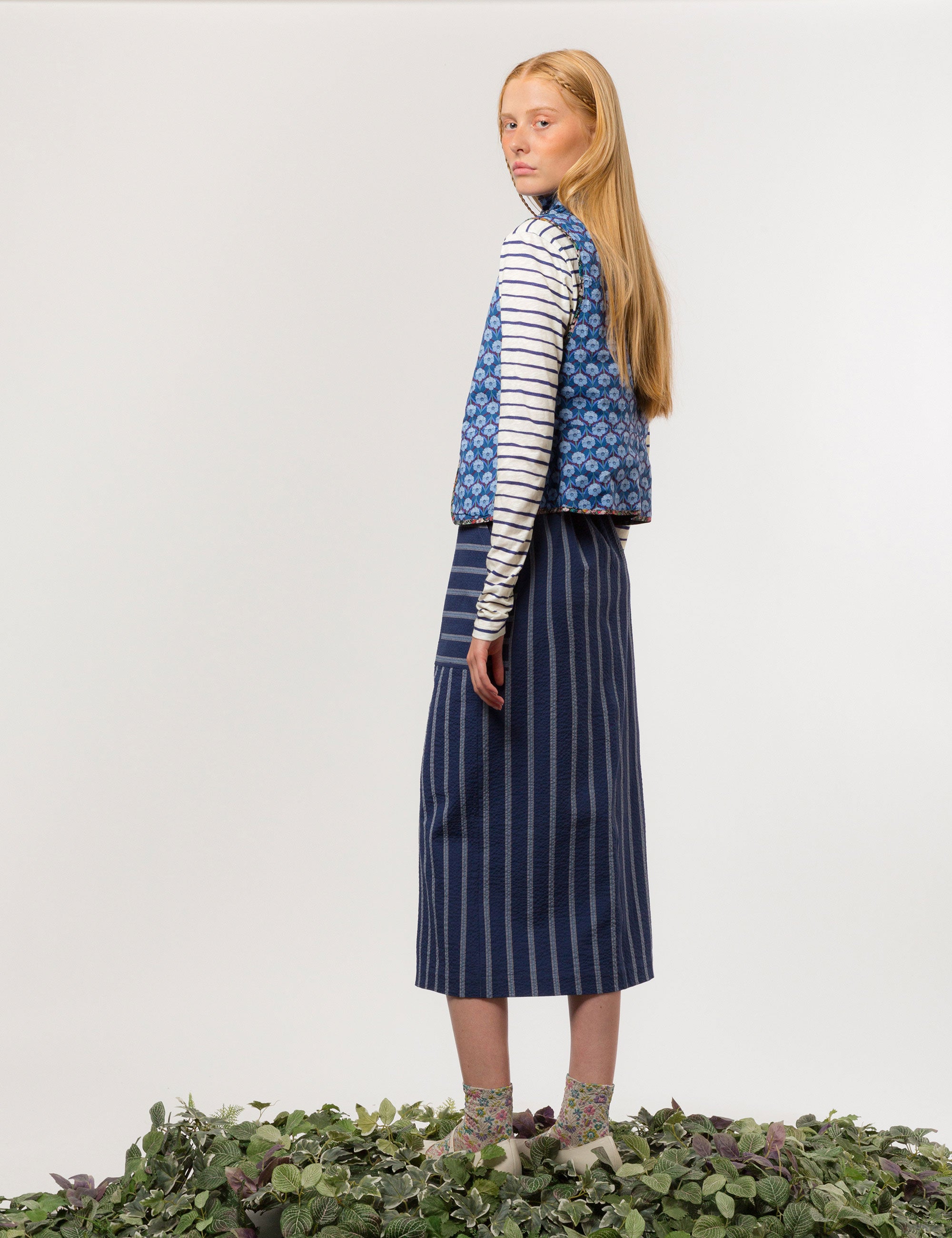 Woman in long sleeved white and blue striped cotton jersey t-shirt, blue and white striped skirt and blue flower patterned vest