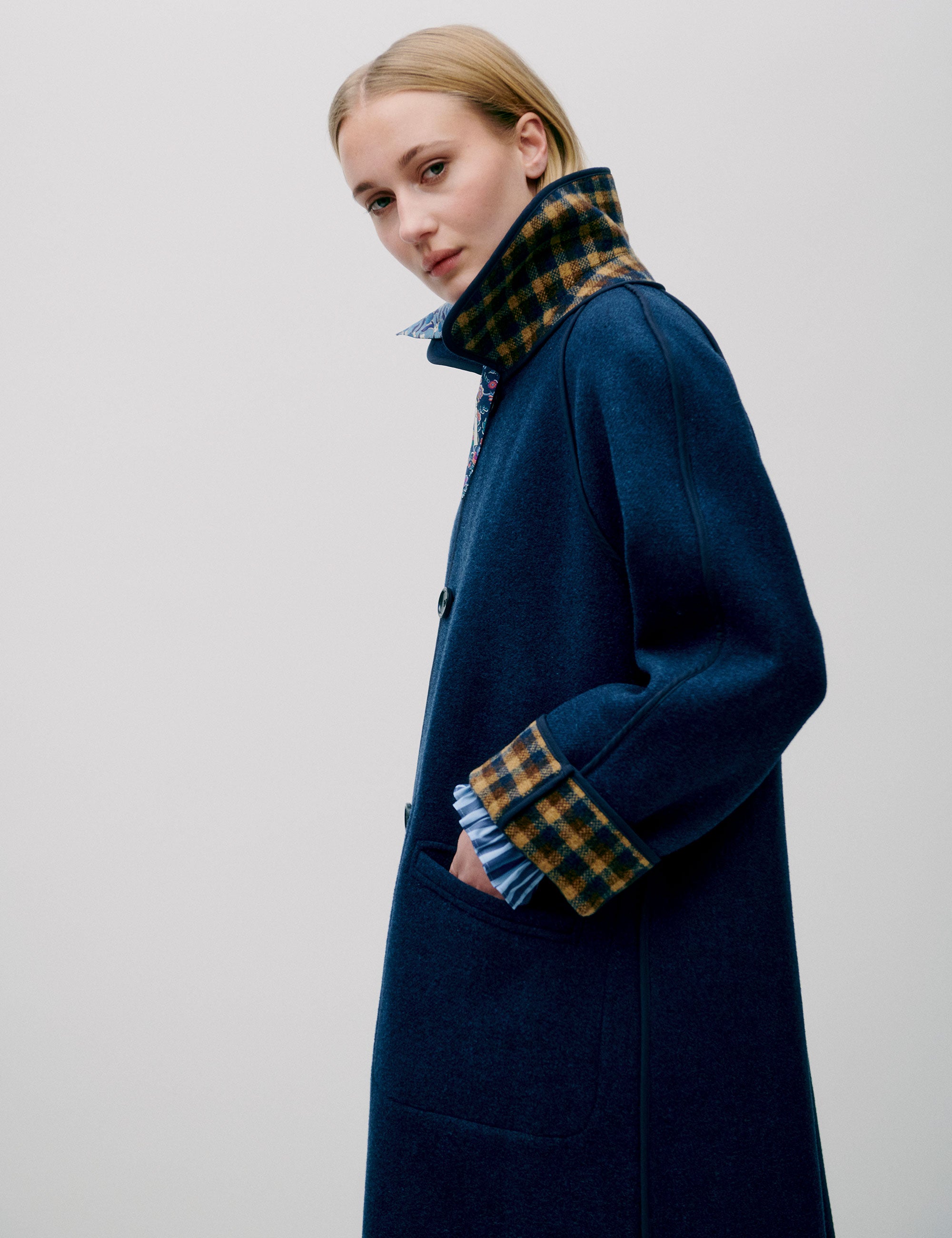 Woman in long blue wool coat with large buttons and collar with check print lining