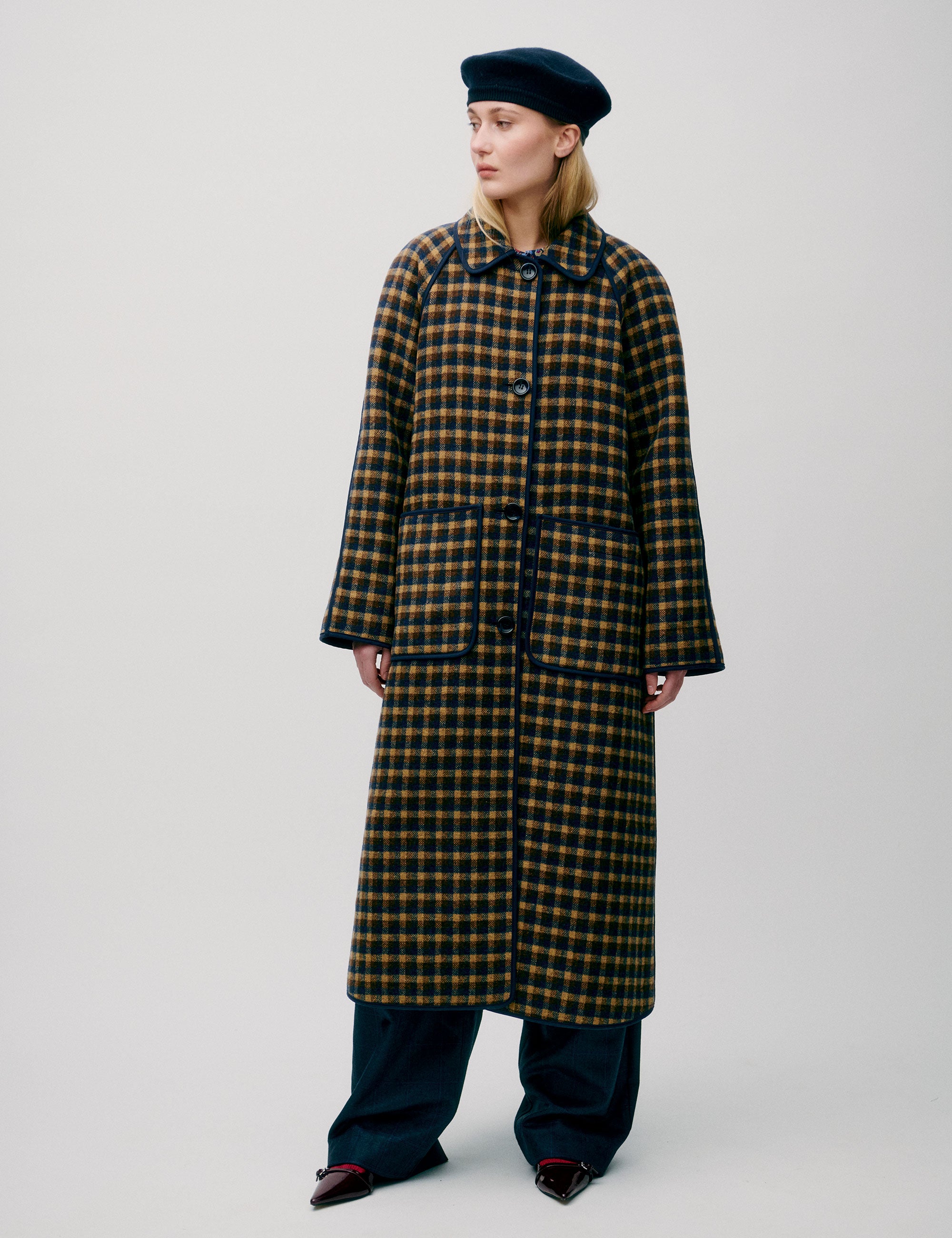 Woman in check print wool coat with large buttons, pockets and collar wearing a beret