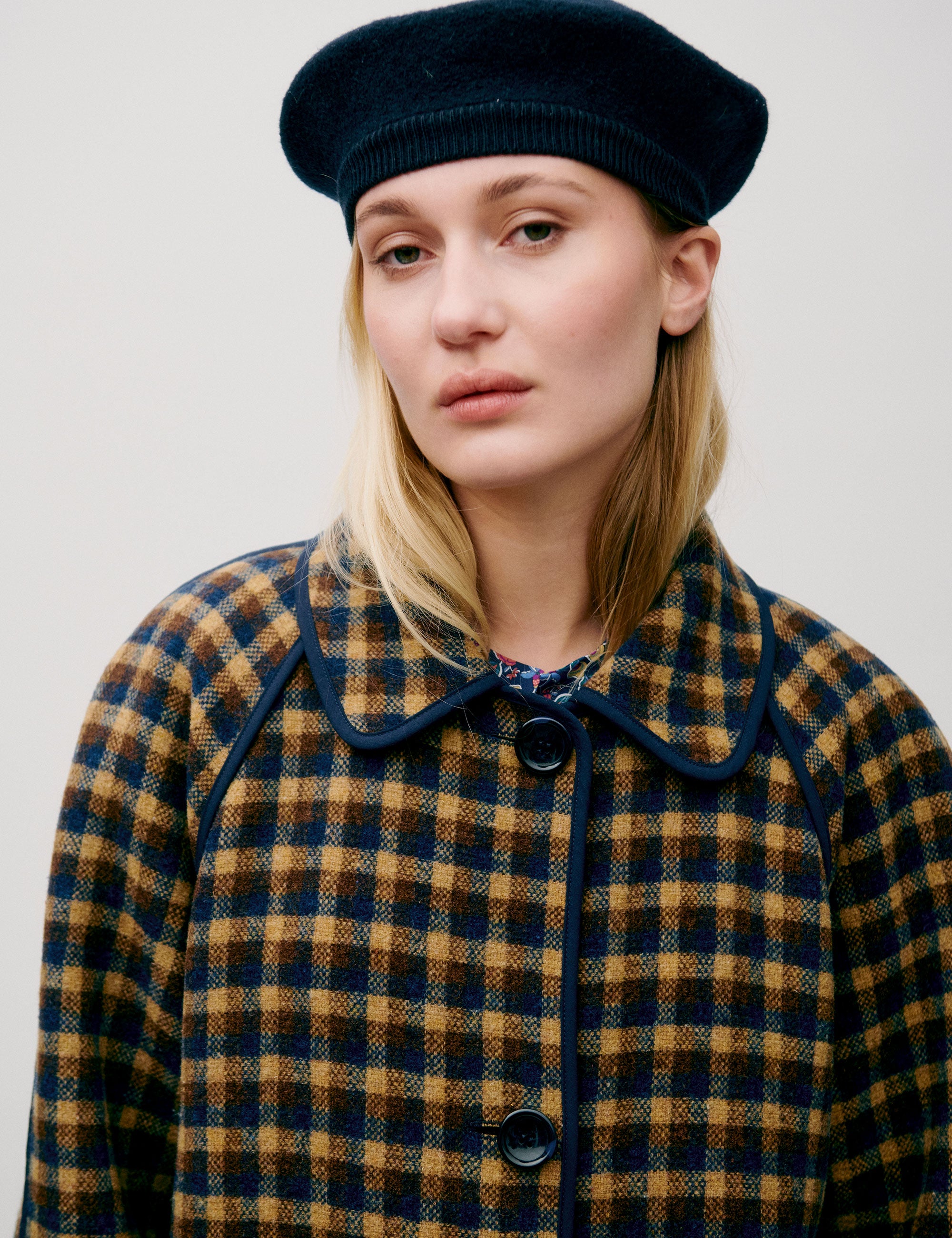 Woman in check print wool coat with large buttons, pockets and collar wearing a beret