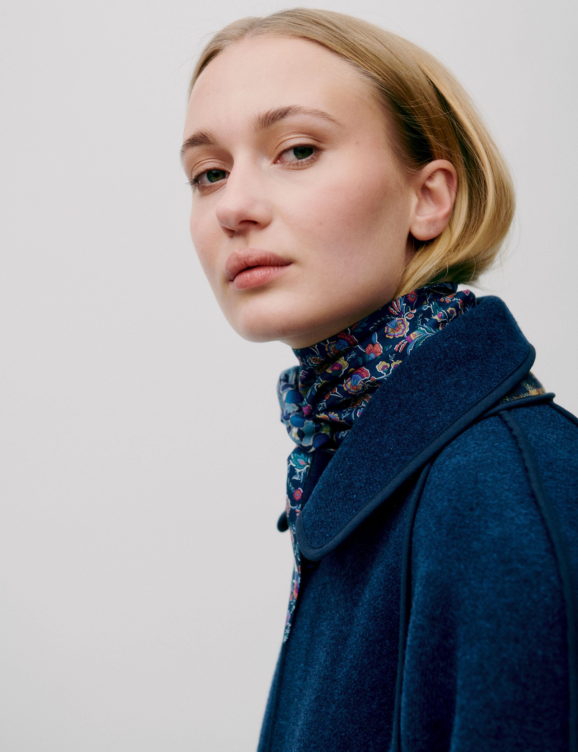 Close-up of woman wearing a floral scarf tied around the neck, styled with a dark blue wool coat