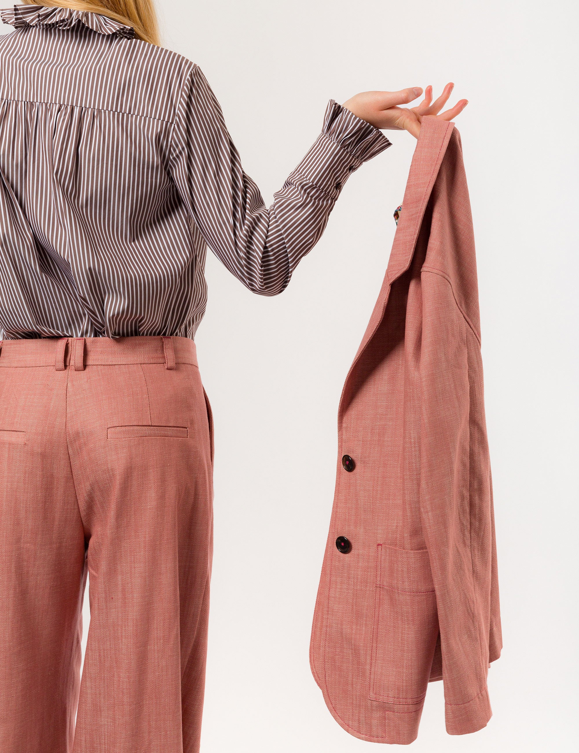Woman in pink suit and brown and white striped shirt with ruffled collar