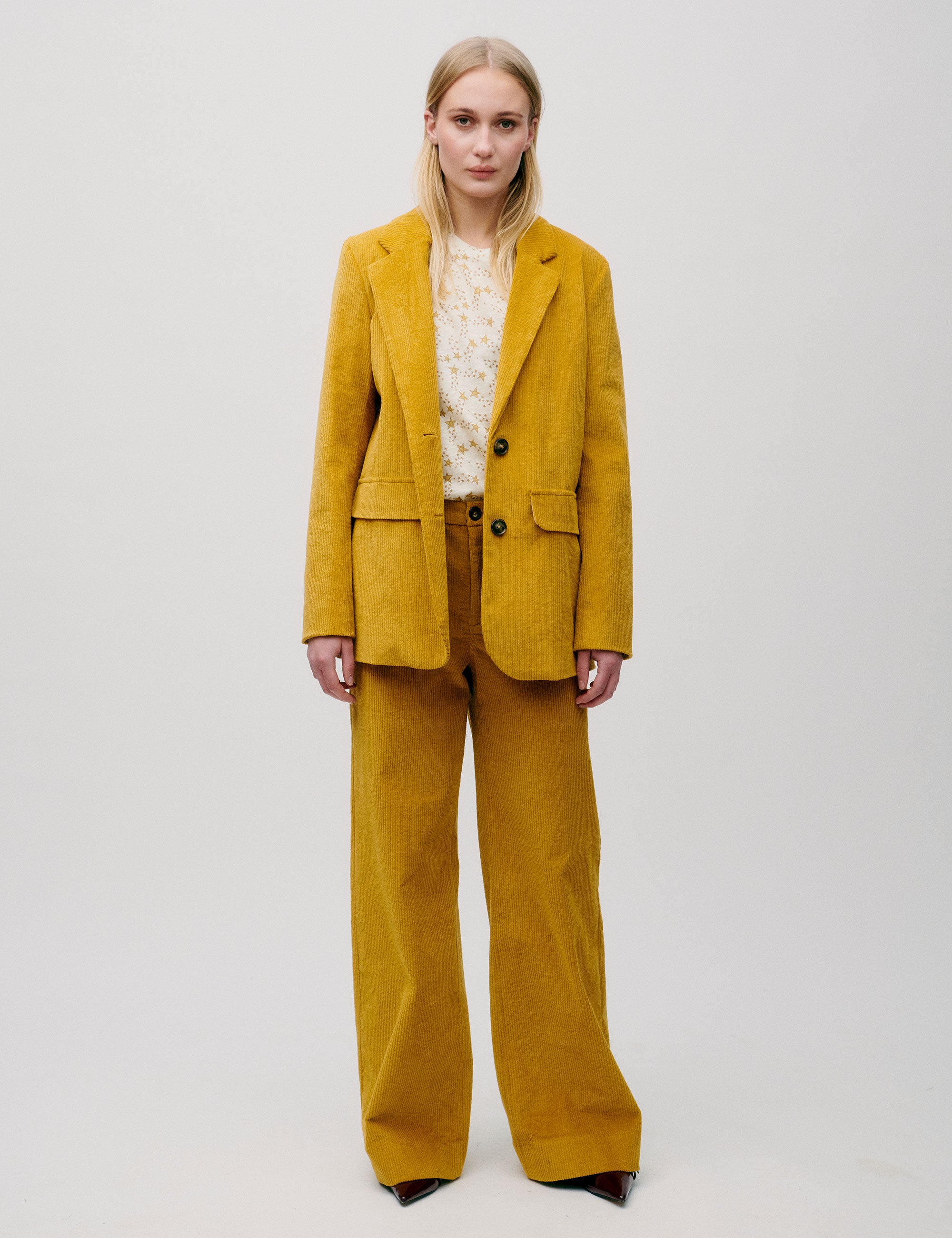 Woman wearing a mustard yellow corduroy blazer with two-button closure, styled with matching trousers and a cream printed t-shirt