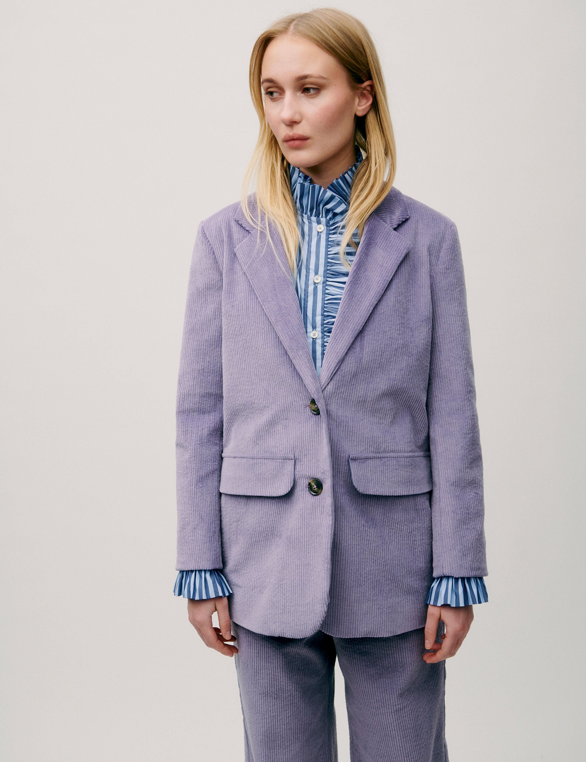 Woman wearing a lilac corduroy blazer with two-button closure and flap pockets, styled over a blue striped blouse
