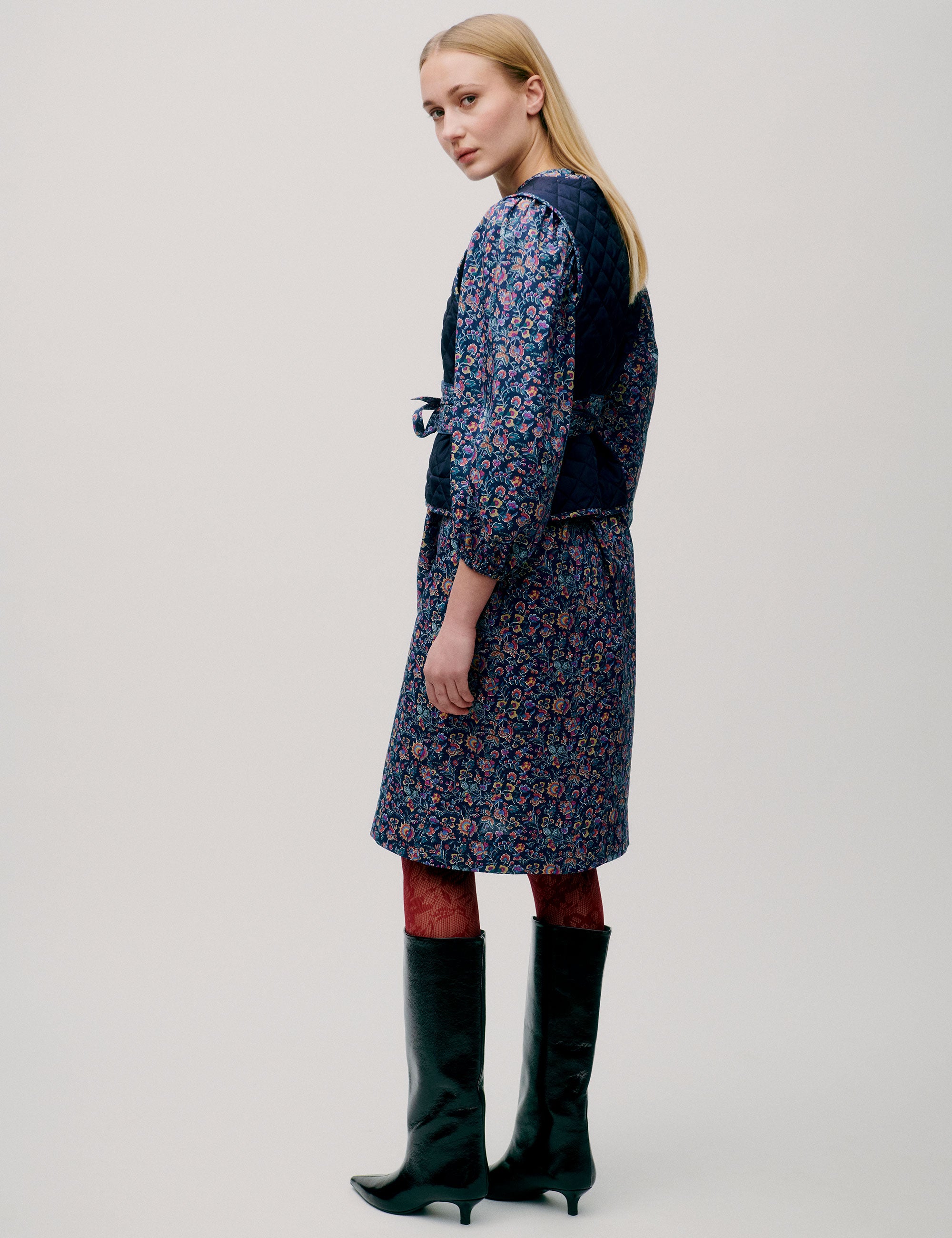 Woman in pink and blue flower patterned short dress with long sleeves, quilted vest and matching cotton belt