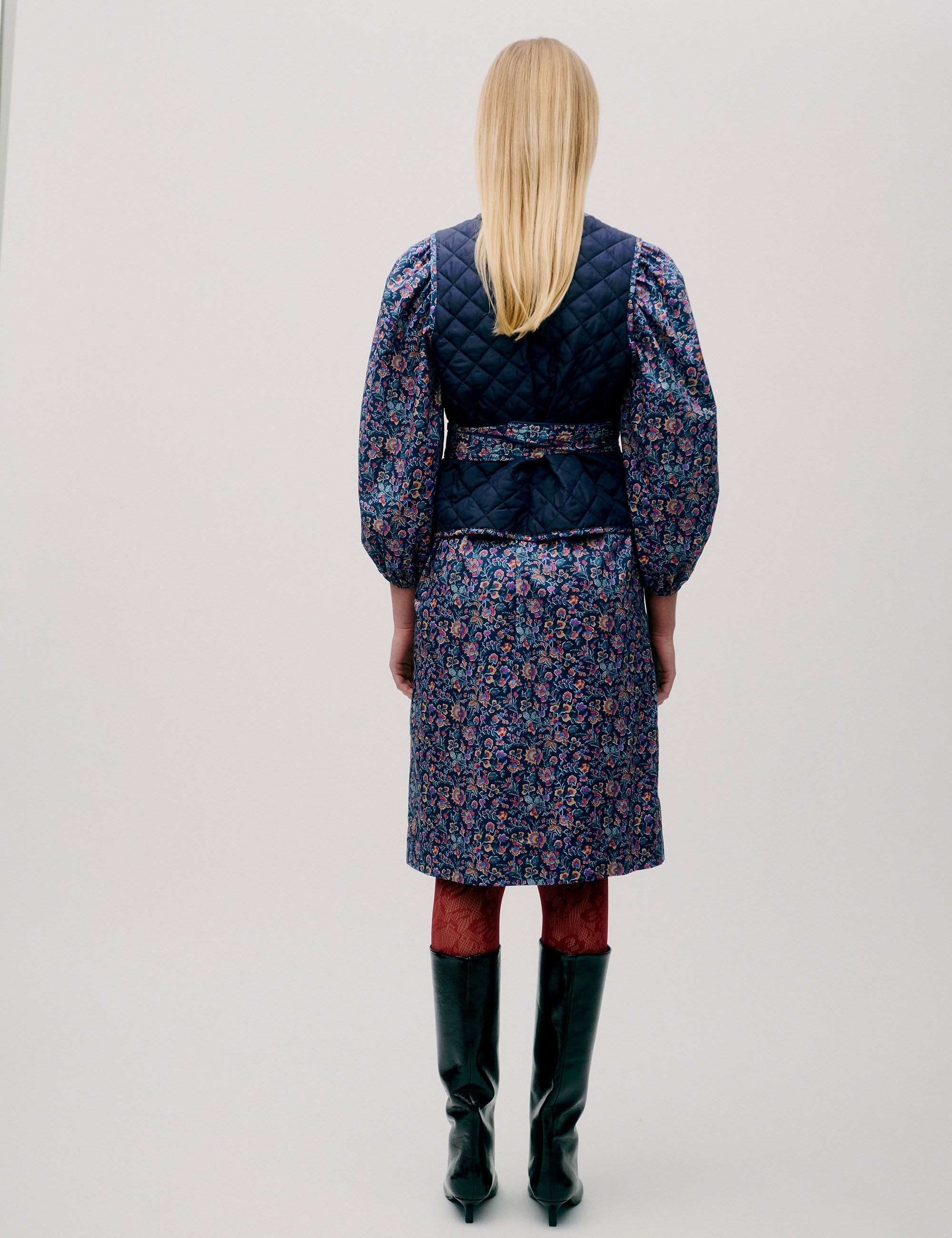 Woman in pink and blue flower patterned short dress with long sleeves, quilted vest and matching cotton belt