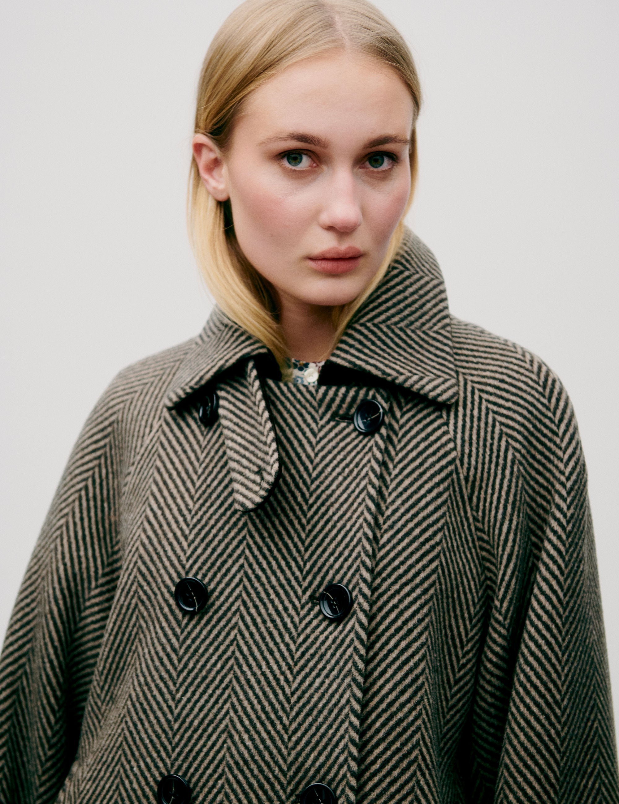 Woman in herringbone patterned green wool jacket with collar, double buttons and pockets