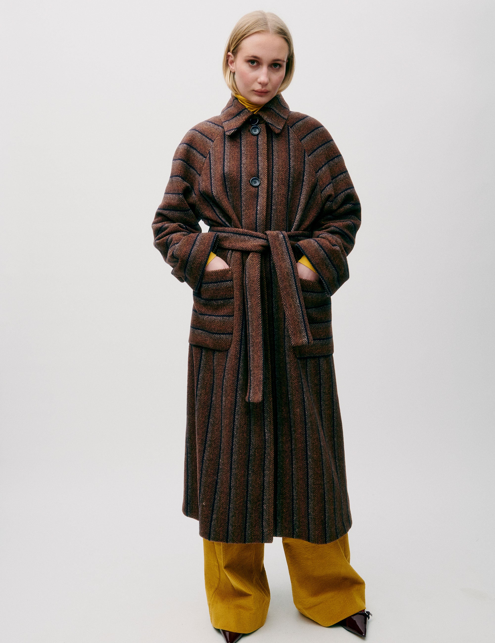 Woman in long wool coat with black and brown stripes, belt, pockets, button and a collar