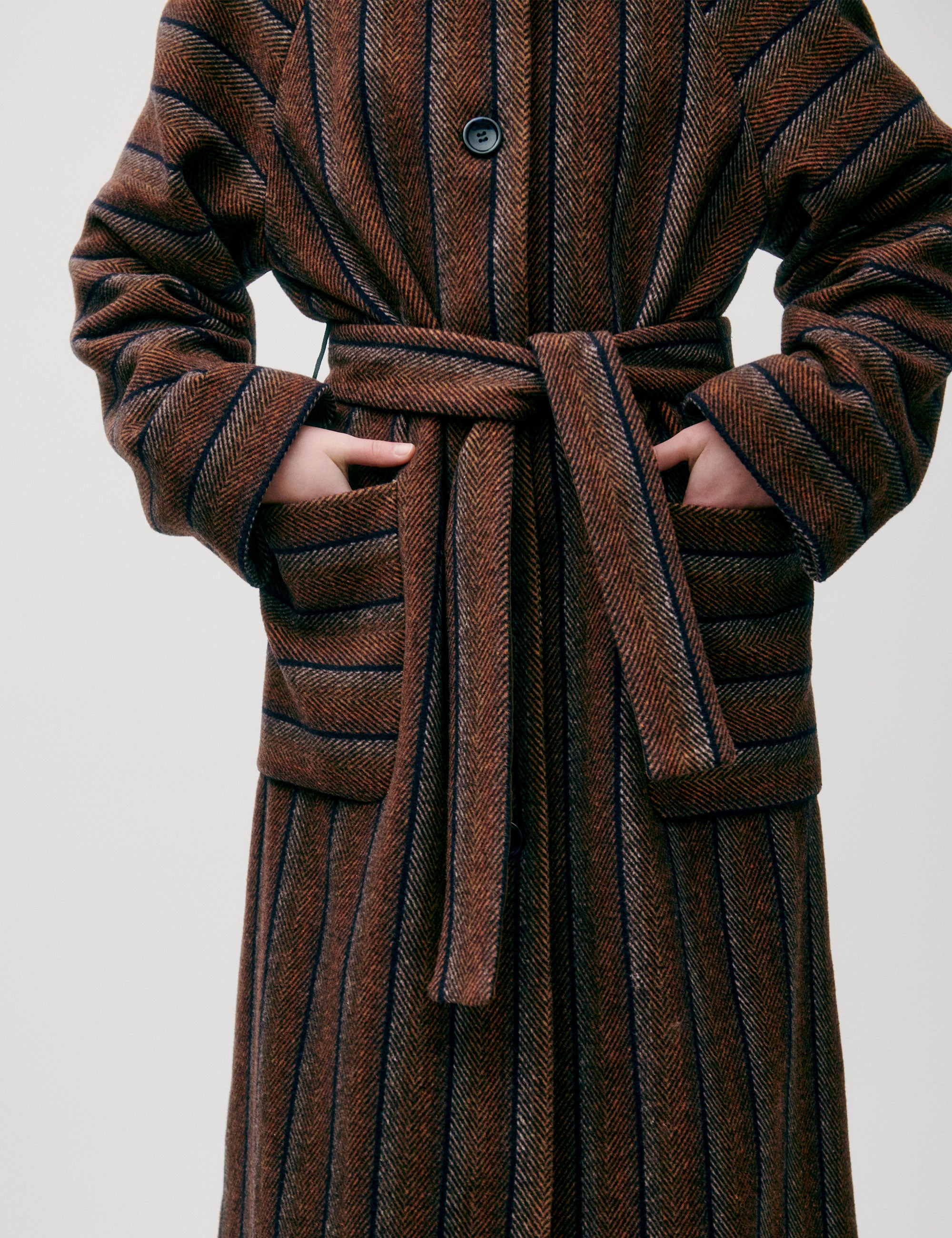 Woman in long wool coat with black and brown stripes, belt, pockets, button and a collar