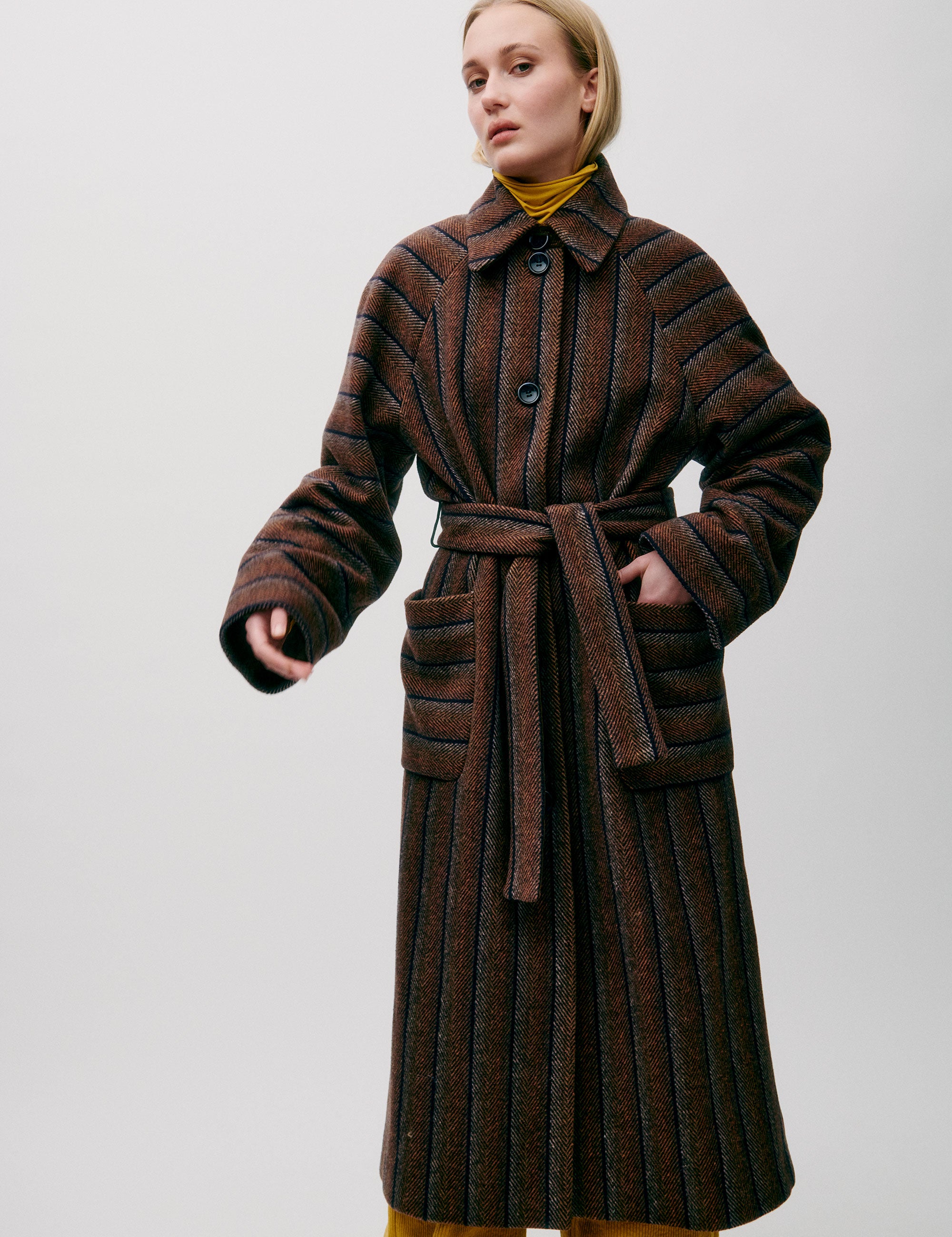 Woman in long wool coat with black and brown stripes, belt, pockets, button and a collar