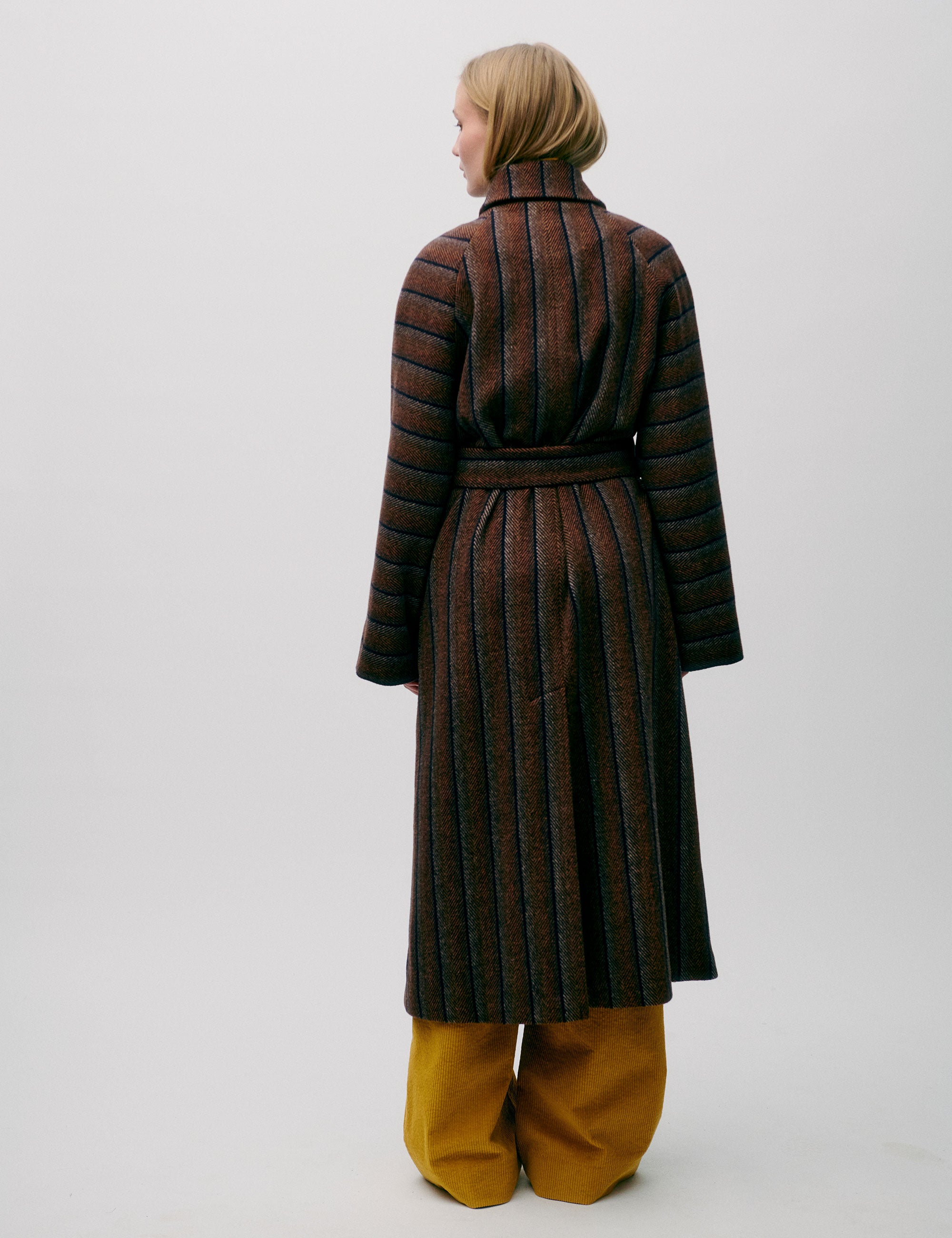 Woman in long wool coat with black and brown stripes, belt, pockets, button and a collar