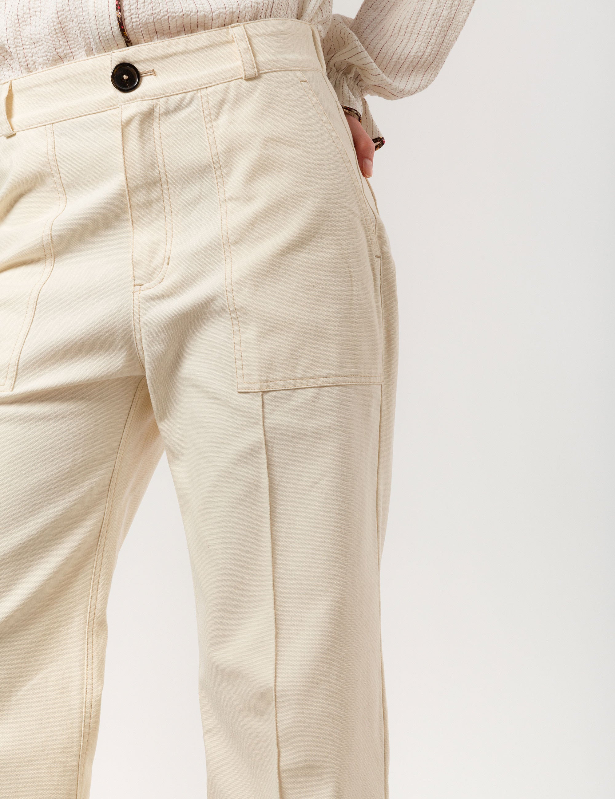 Woman in creme white wide canvas pants and white striped long-sleeved shirt with frilled cuffs