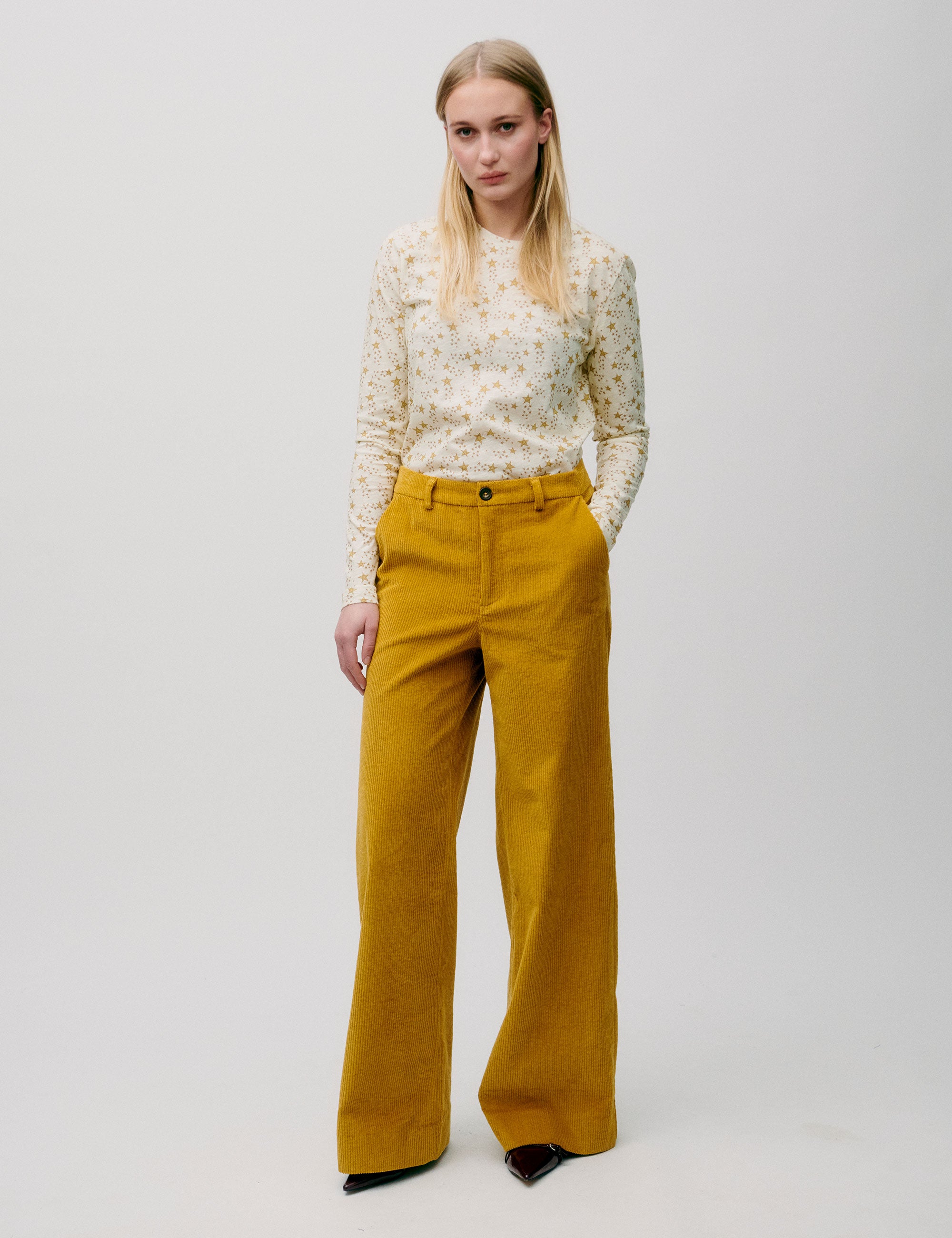 Woman in wide legged corduroy pants in honey yellow color and long-sleeved t-shirt with yellow star pattern