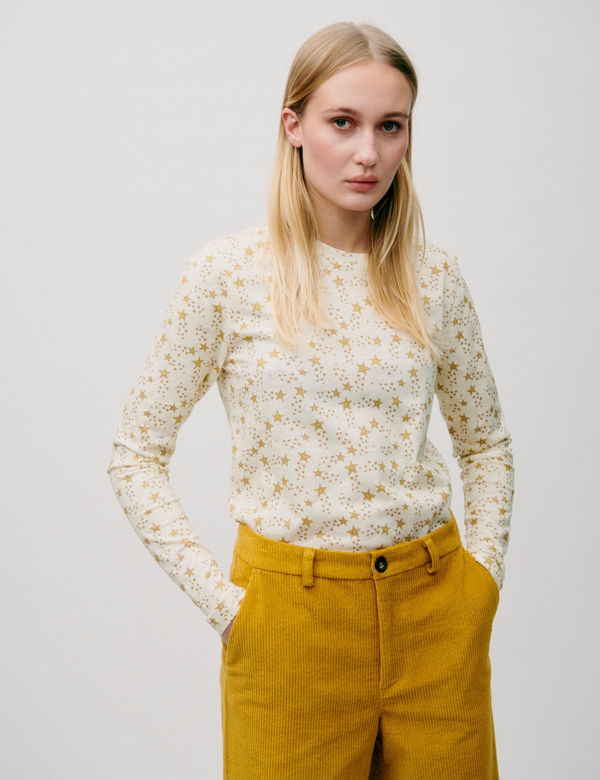 Woman wearing a cream long-sleeve top with gold star print, paired with mustard yellow corduroy trousers