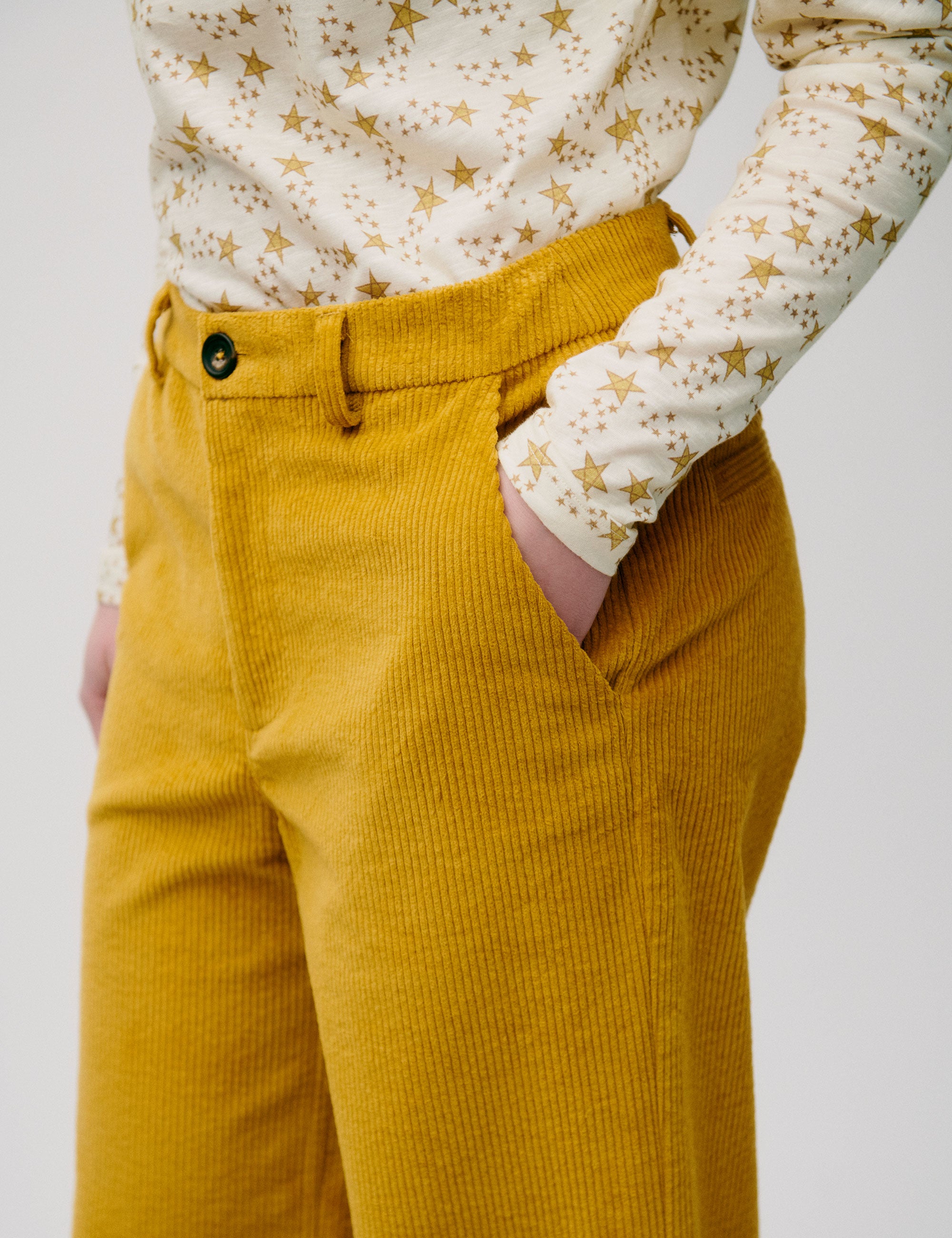 Woman in wide legged corduroy pants in honey yellow color and long-sleeved t-shirt with yellow star pattern