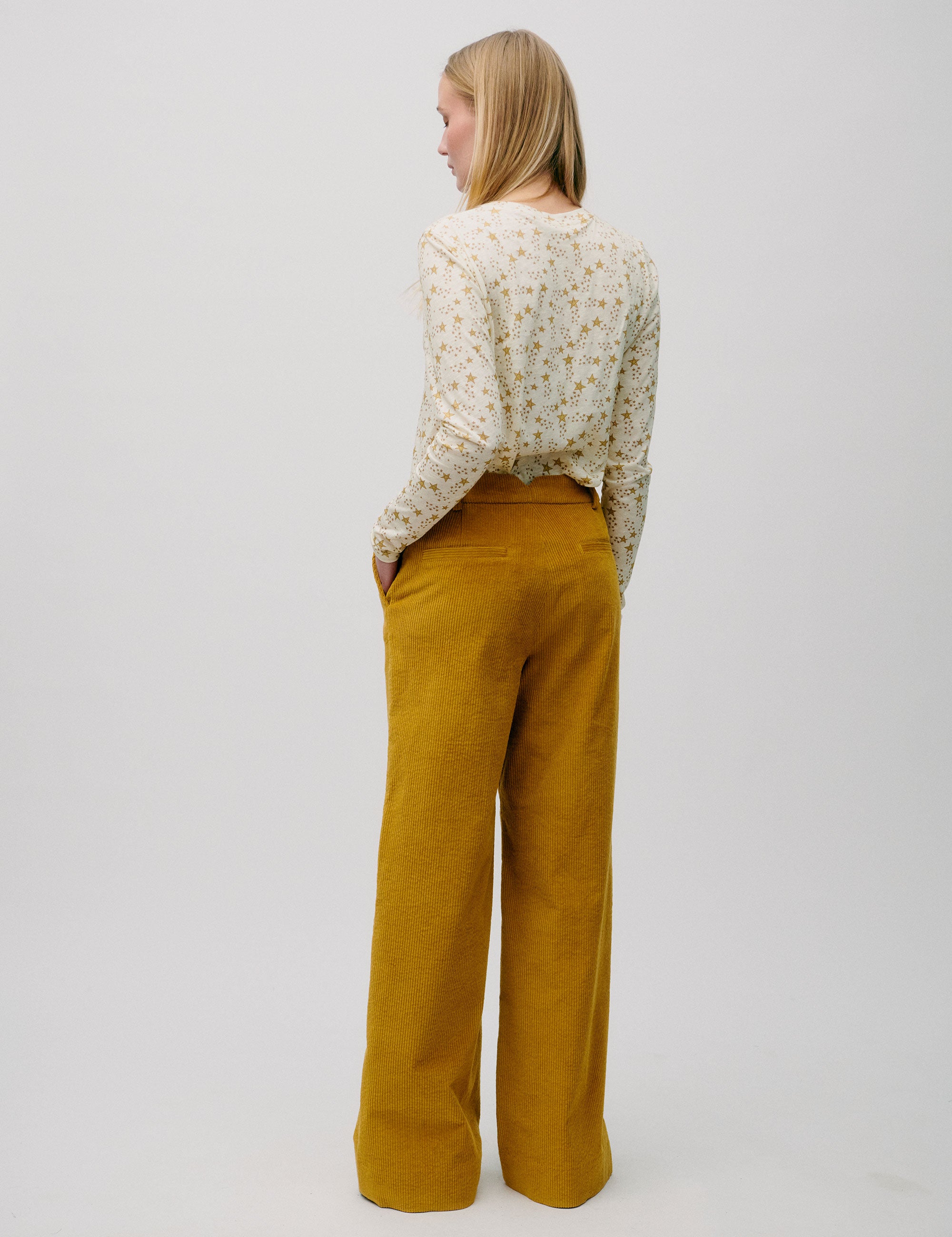 Woman in wide legged corduroy pants in honey yellow color and long-sleeved t-shirt with yellow star pattern