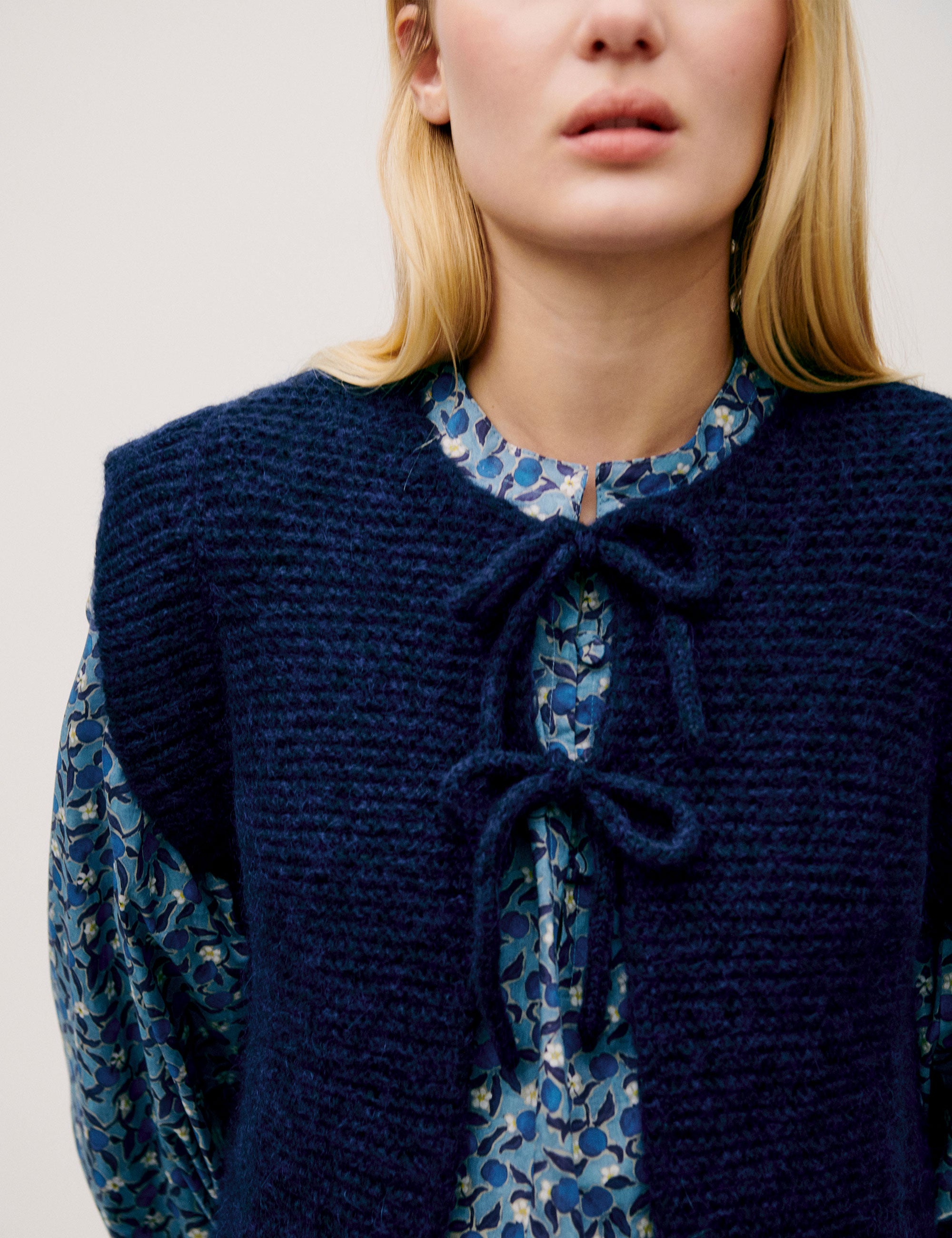 Woman in long sleeved dress with blue flower pattern and dark blue knitted wool vest